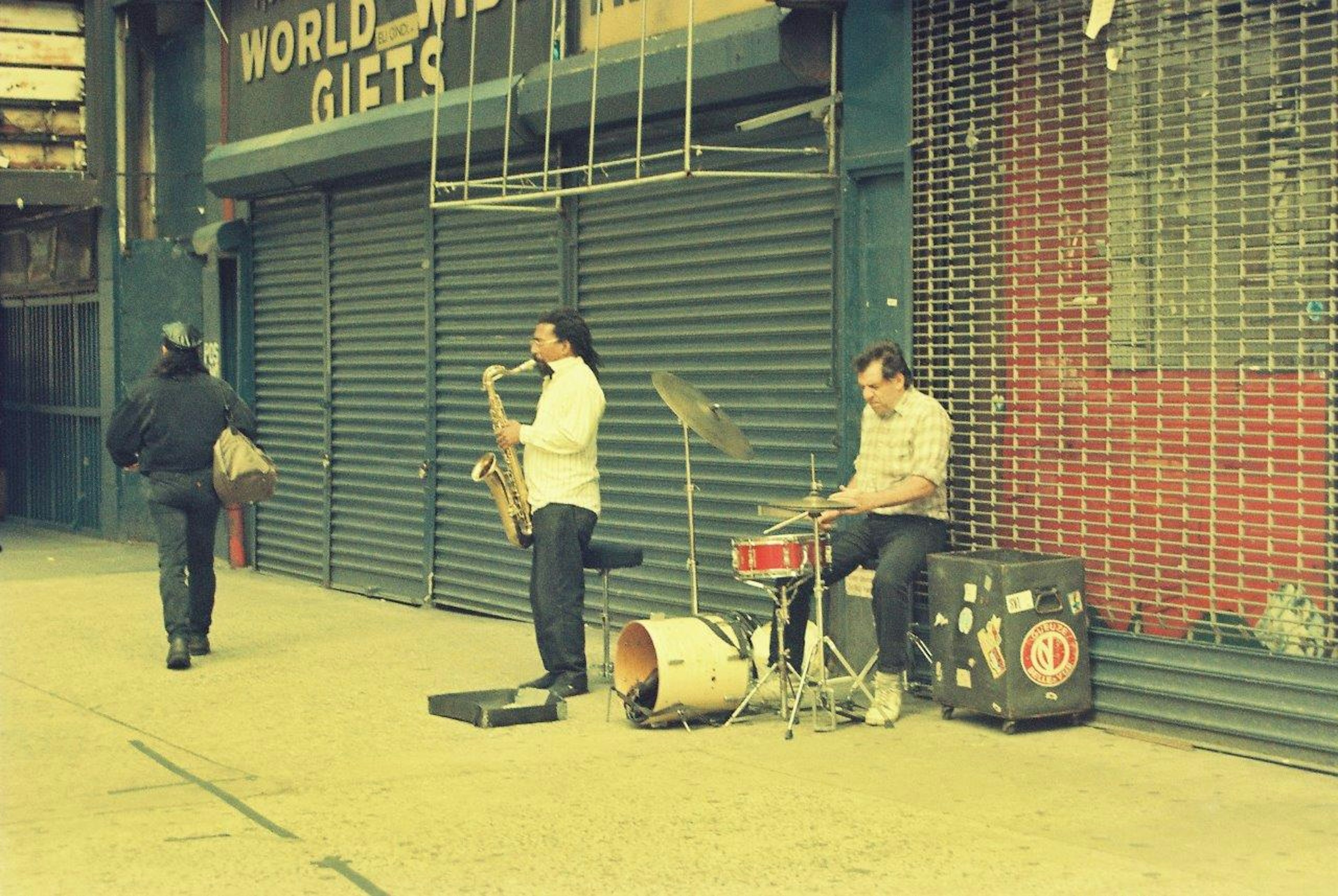 A man playing saxophone and another man playing drums on the street