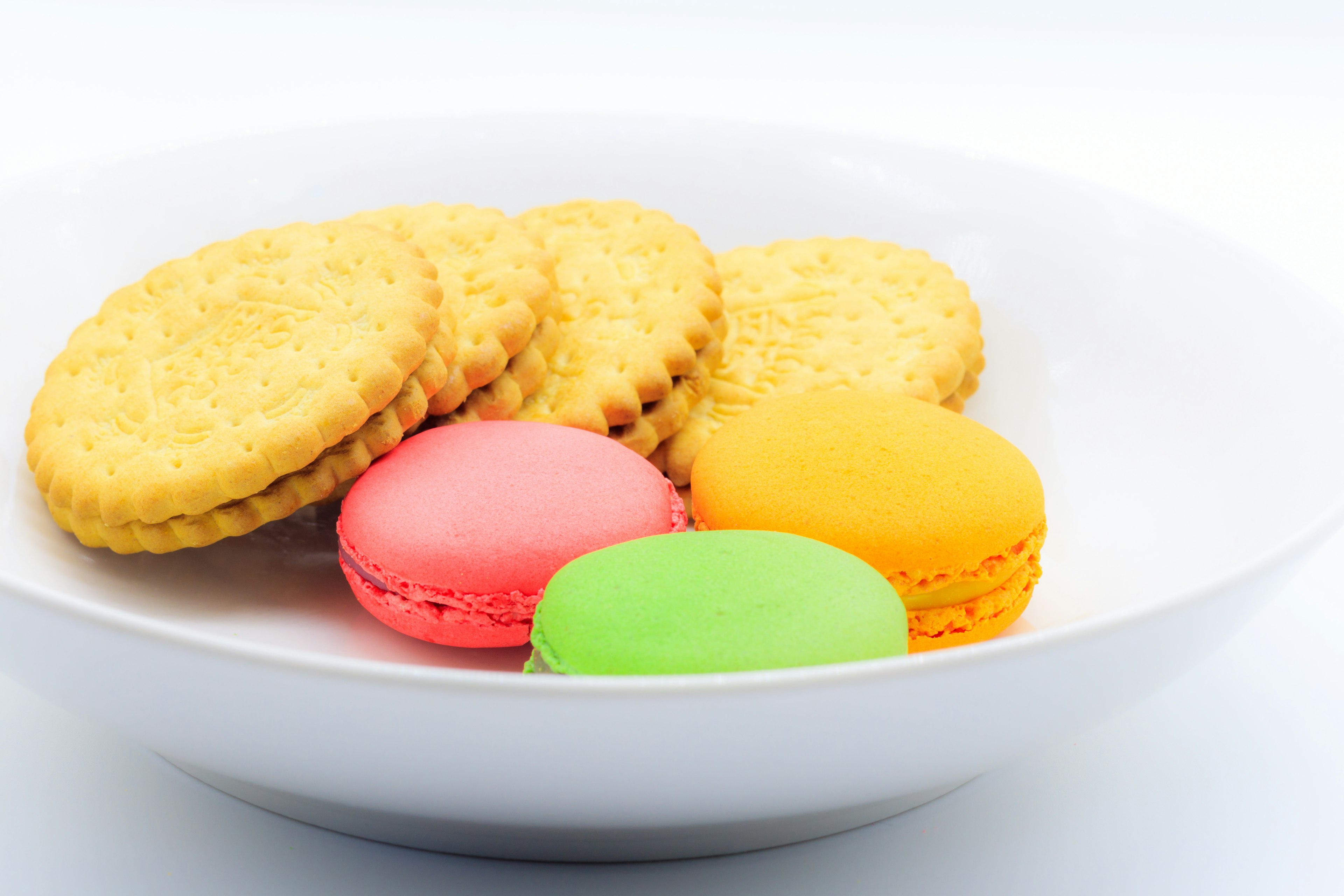 Macaron berwarna dan biskuit disusun di atas piring putih