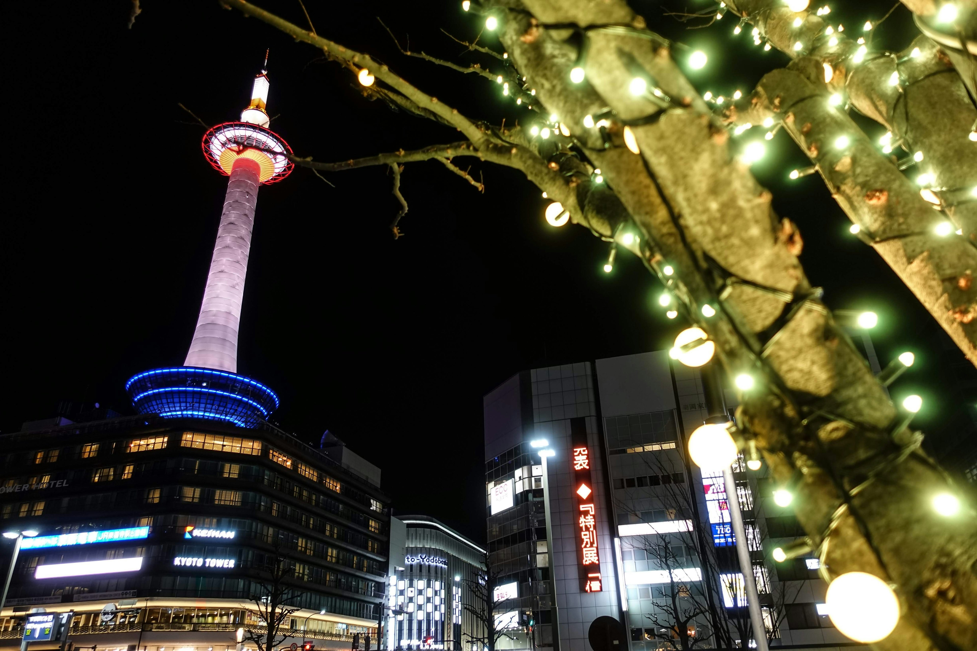 Kyoto Tower illuminated at night with decorative lights on a tree