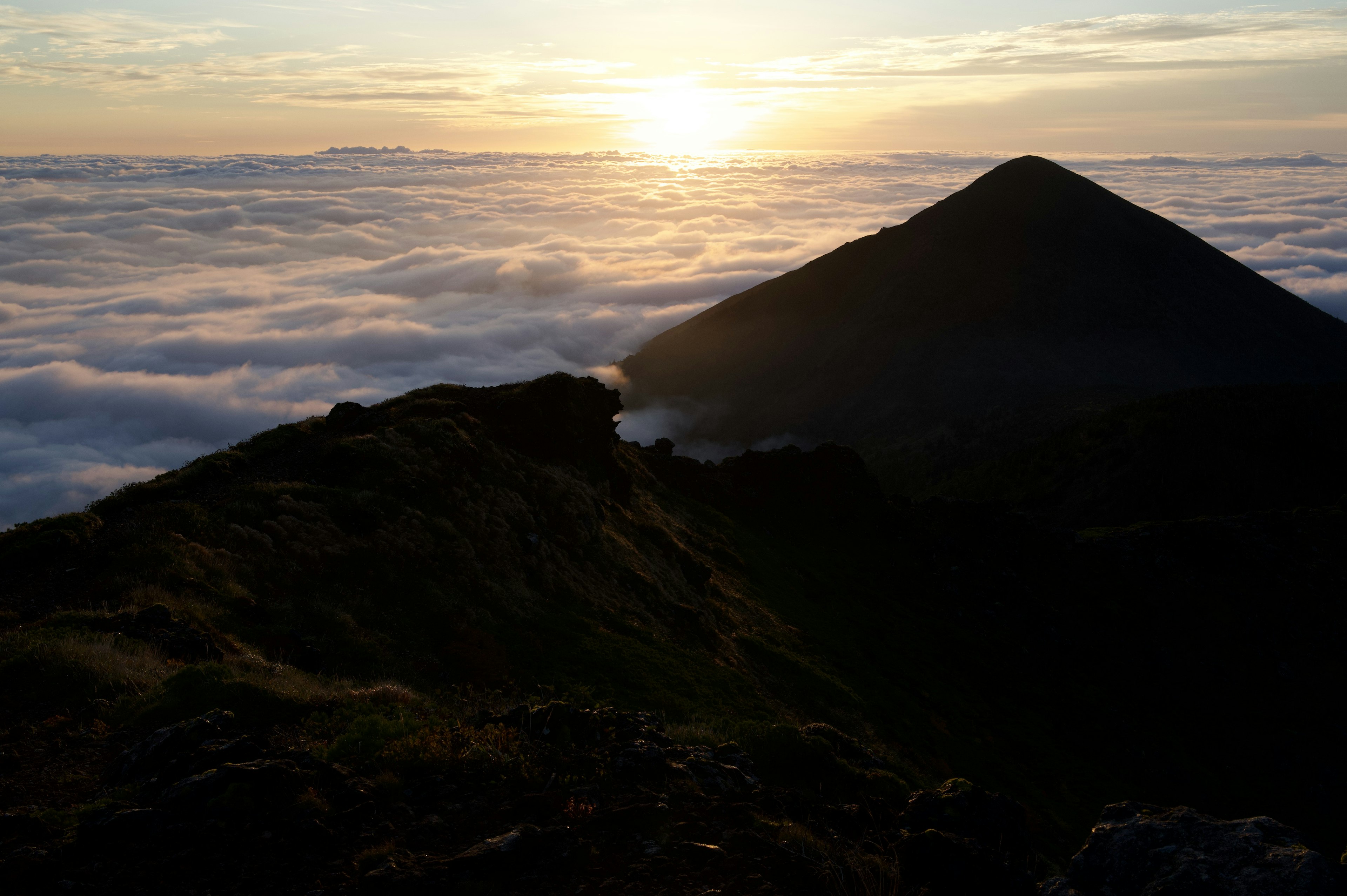 Matahari terbenam di atas lautan awan dengan siluet gunung