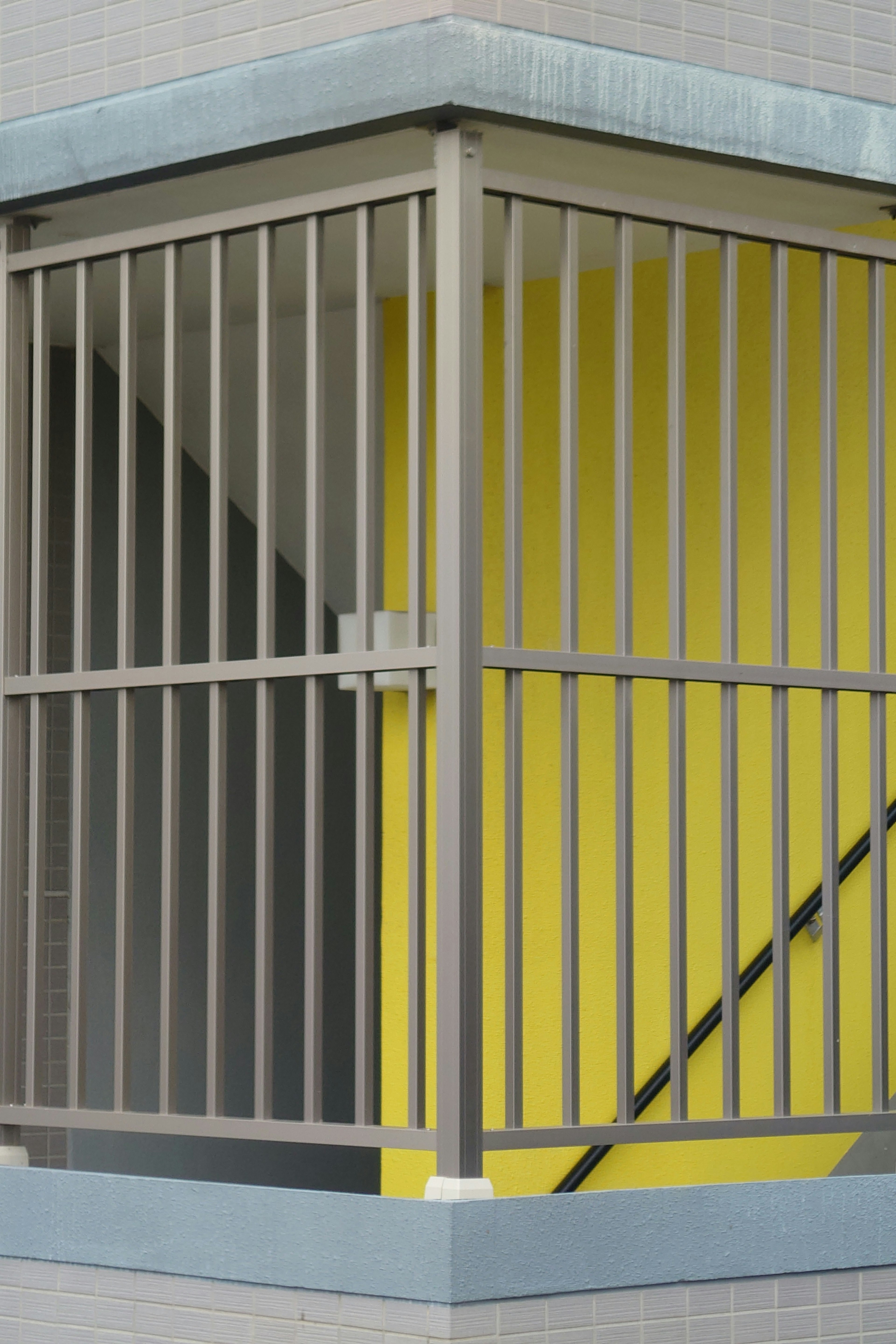 Corner of a staircase with a yellow wall and metal railing