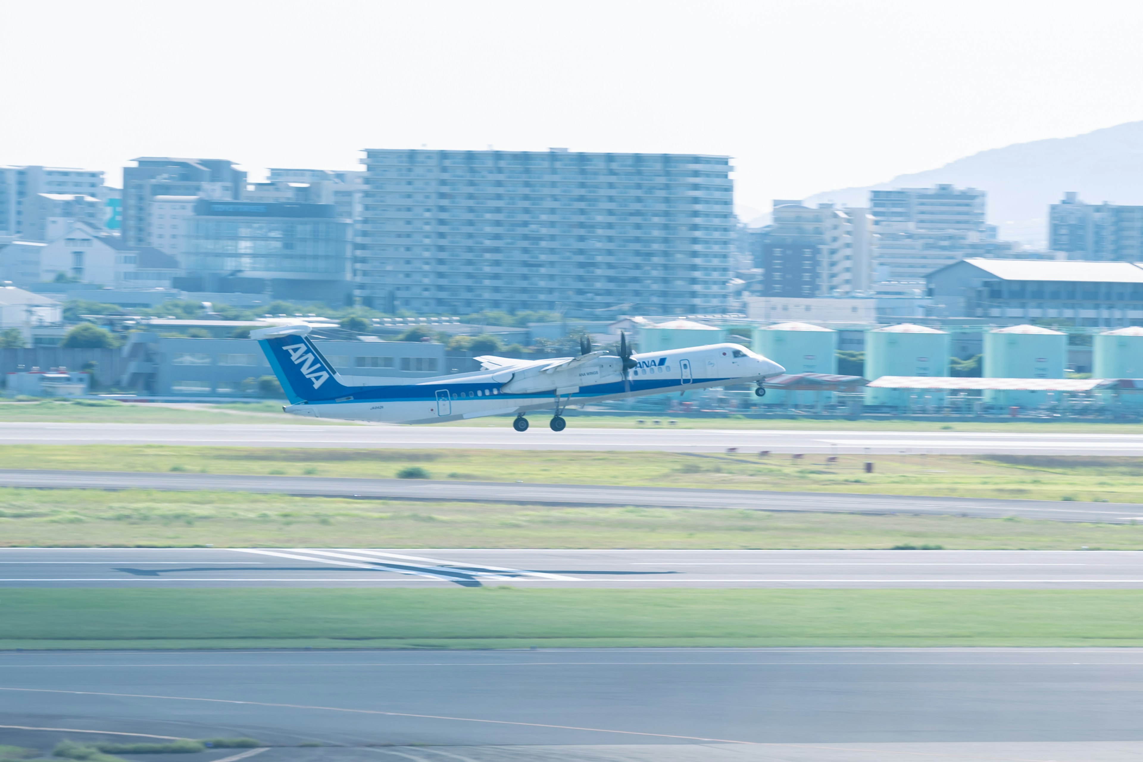 青い飛行機が滑走路に着陸する風景 背景にはビル群が見える