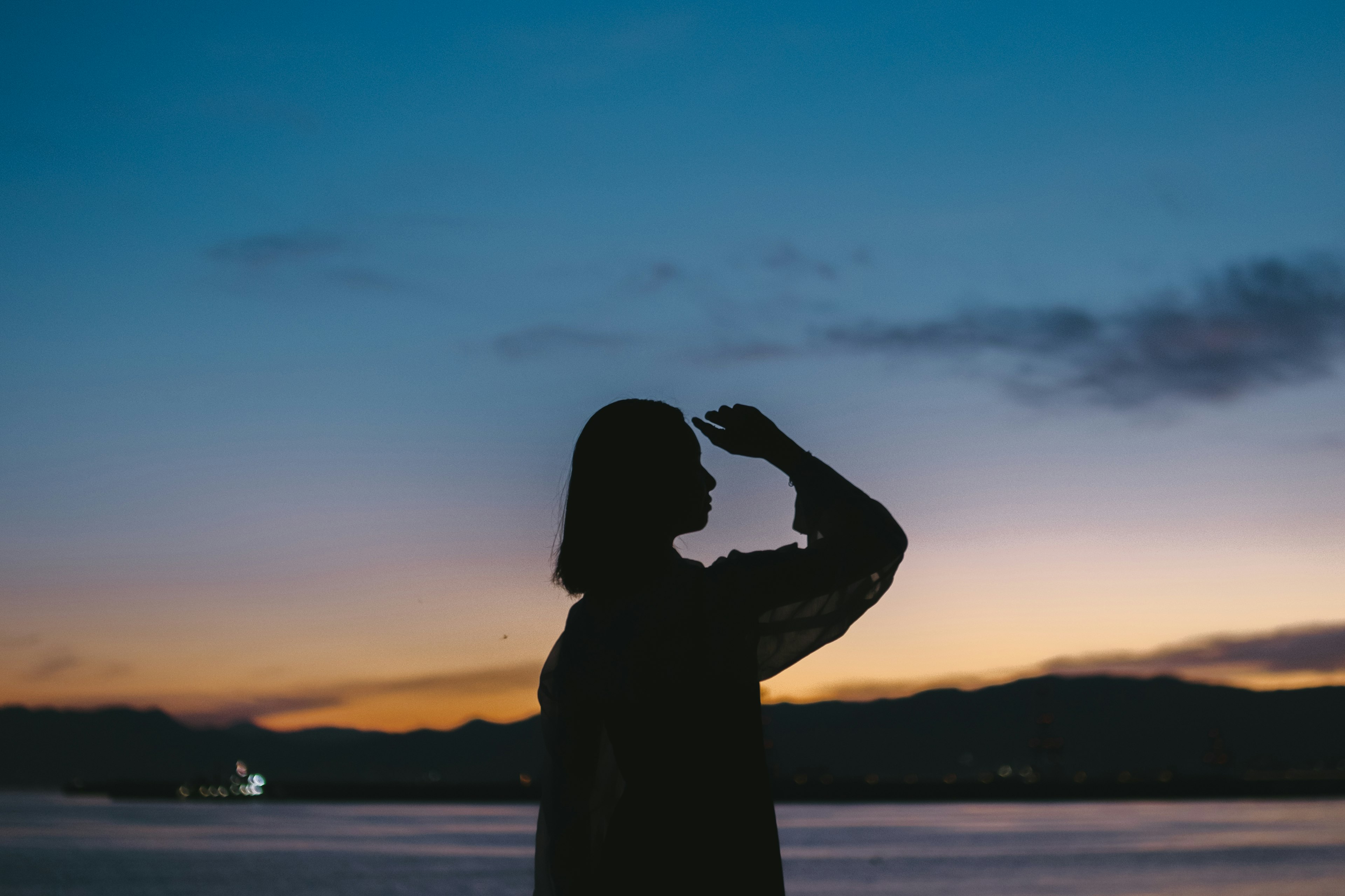 夕焼けを背景にした女性のシルエットが海を見つめている