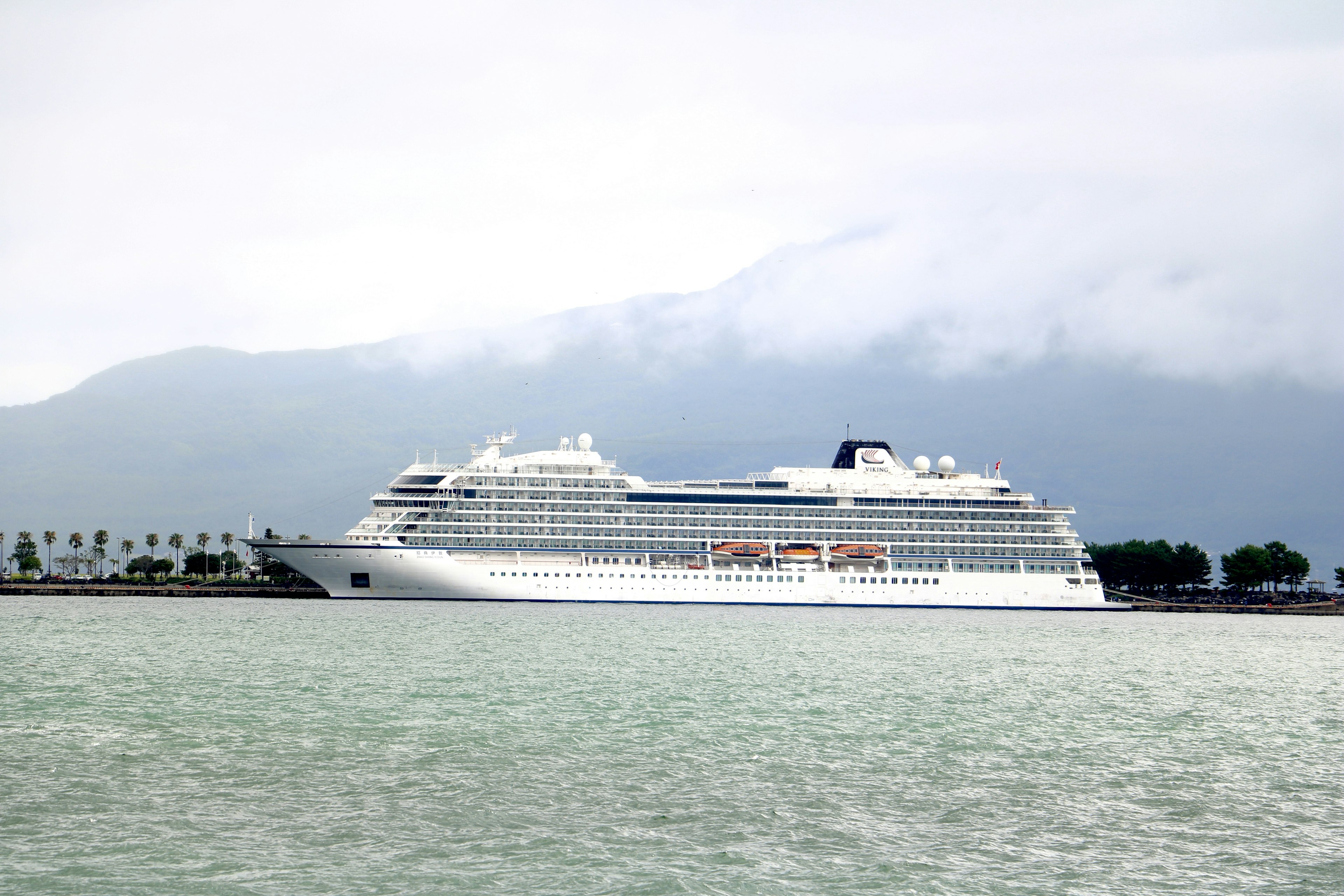 A large cruise ship docked in a harbor with mountains in the background