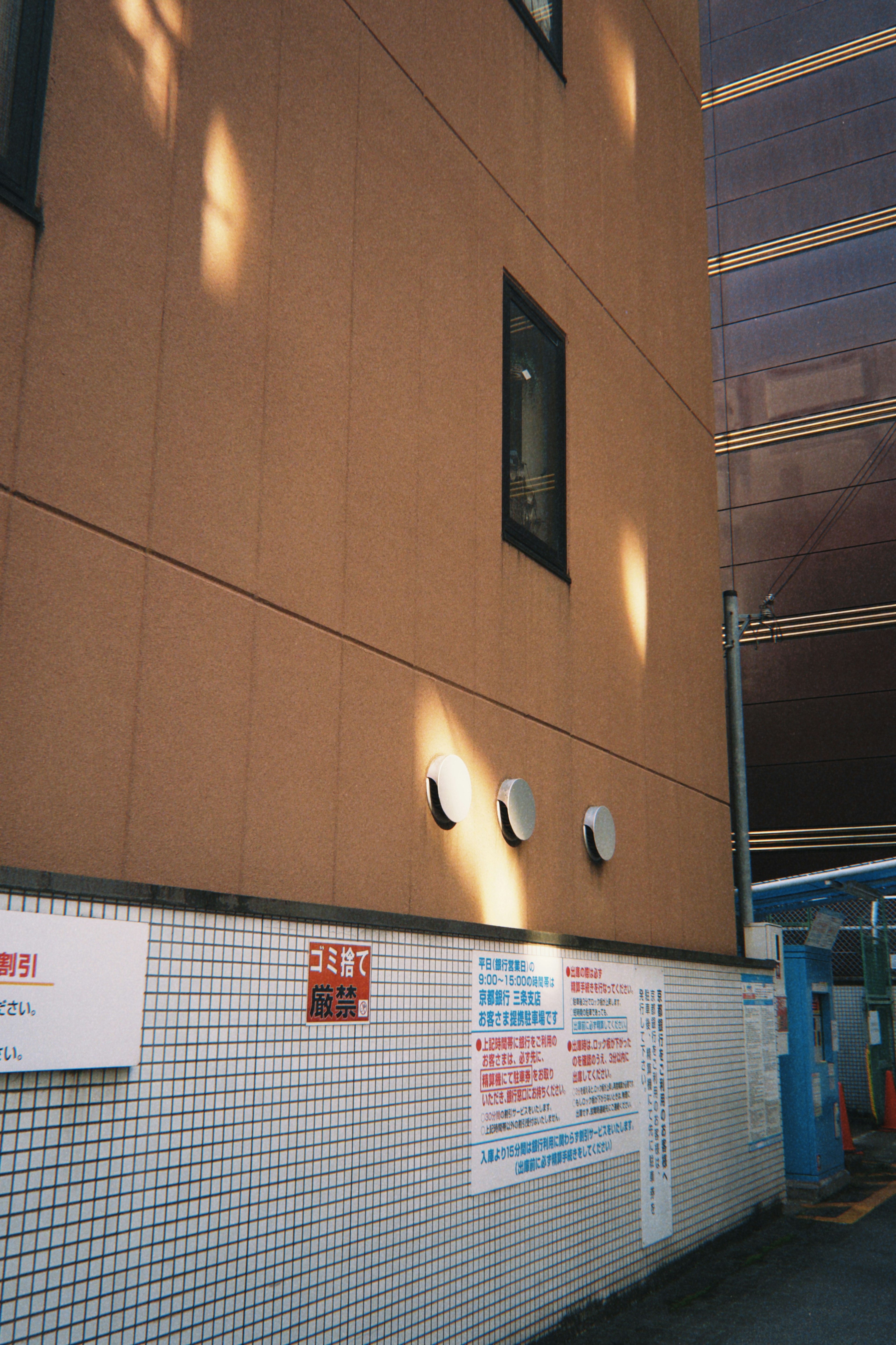 Partie d'un bâtiment avec un mur extérieur orange et un mur carrelé blanc Une fenêtre est visible avec des luminaires fixés au mur