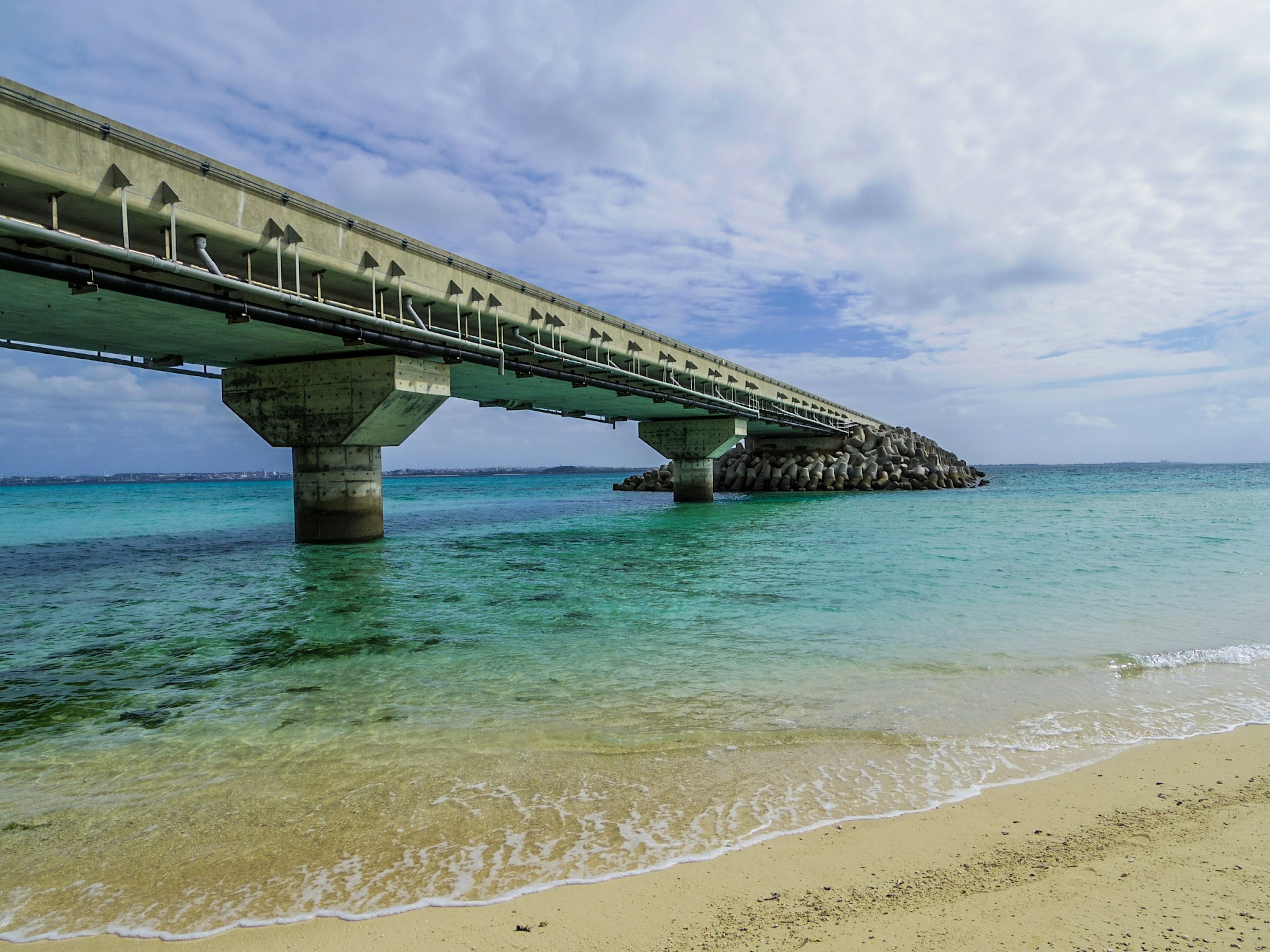 Malerscher Blick auf eine Brücke über klares türkisfarbenes Wasser und Sandstrand