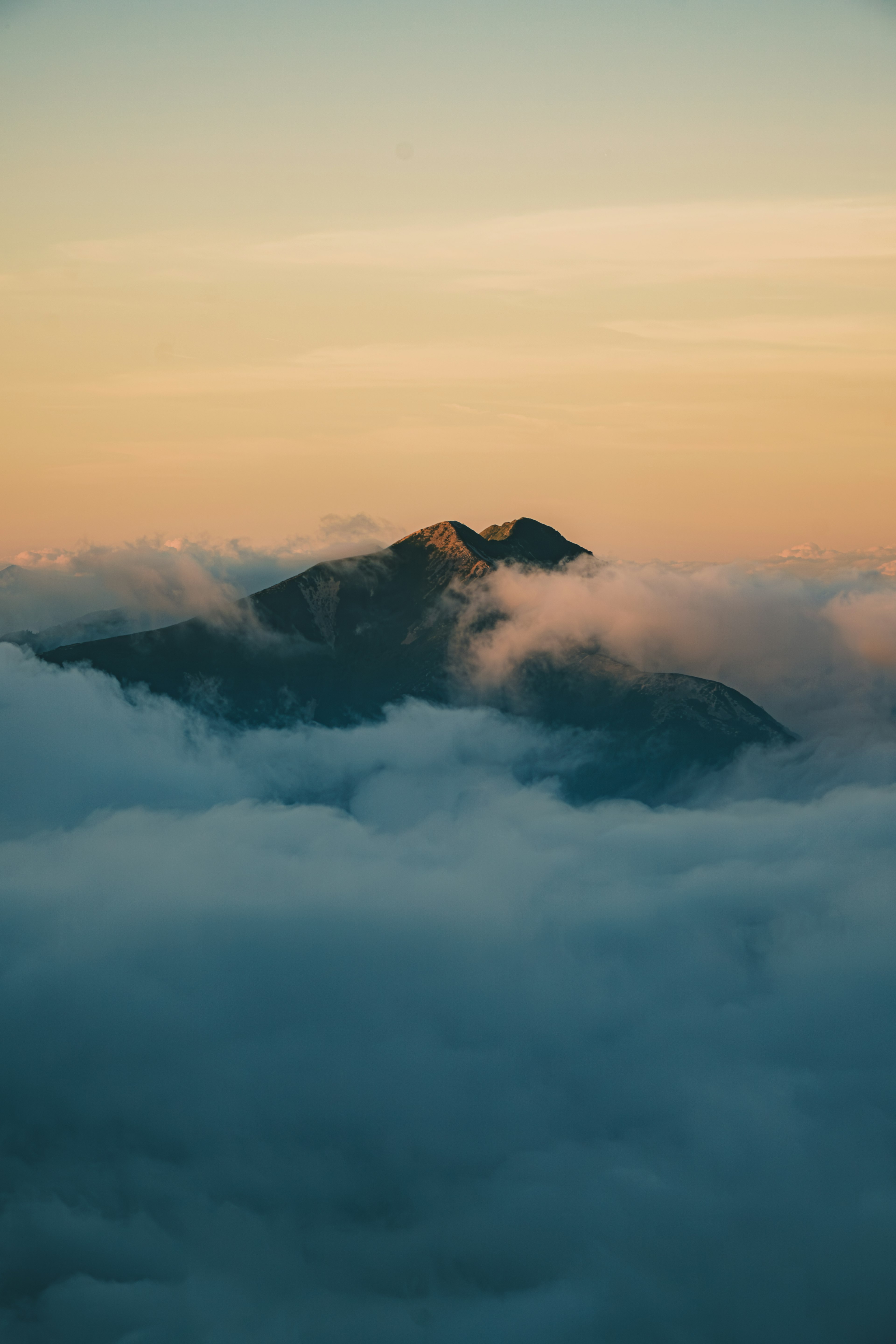 Sebuah gunung yang muncul dari awan saat matahari terbenam dengan warna langit yang cerah