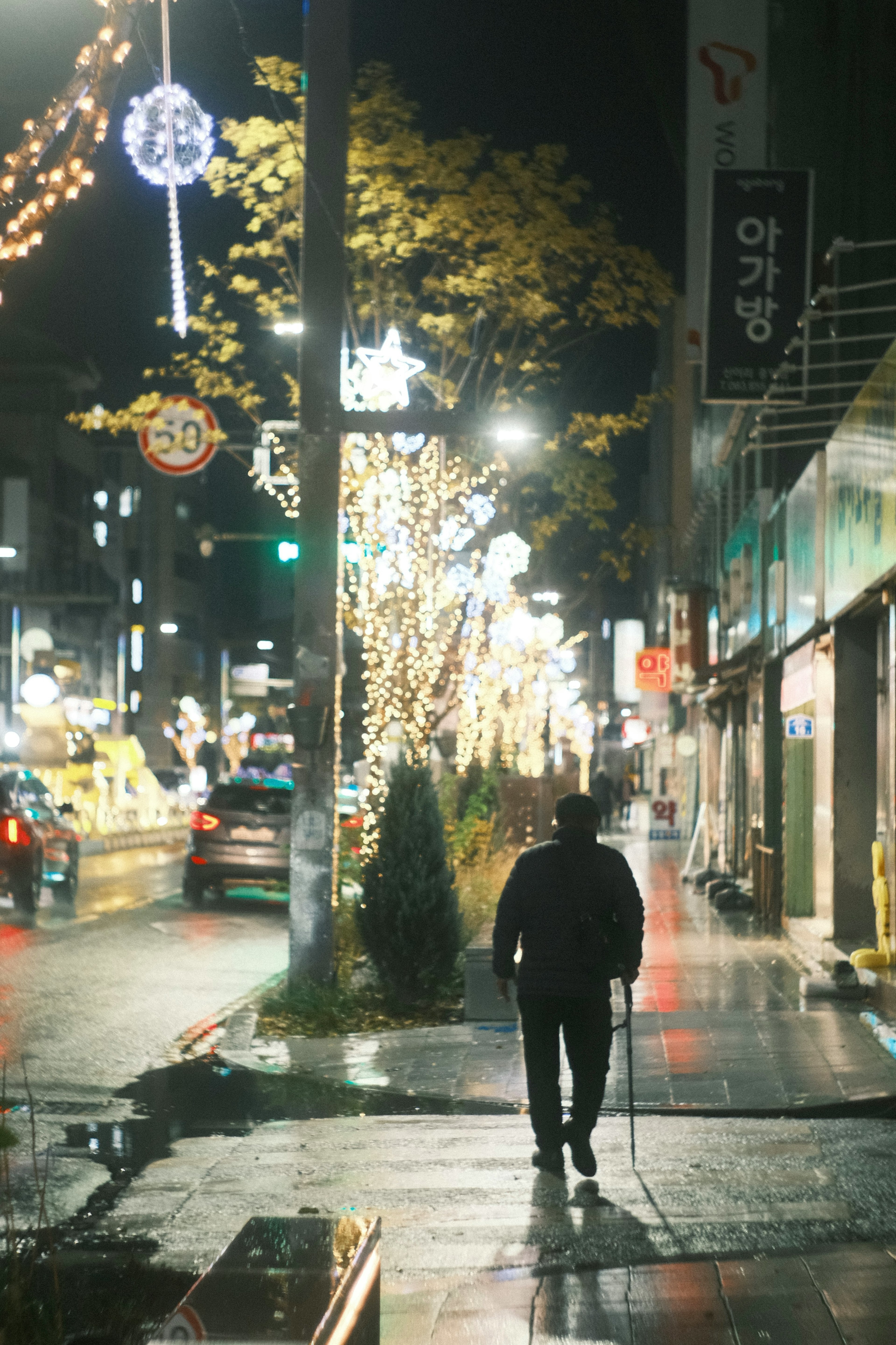 Un uomo che cammina in una strada bagnata di notte con luci festive