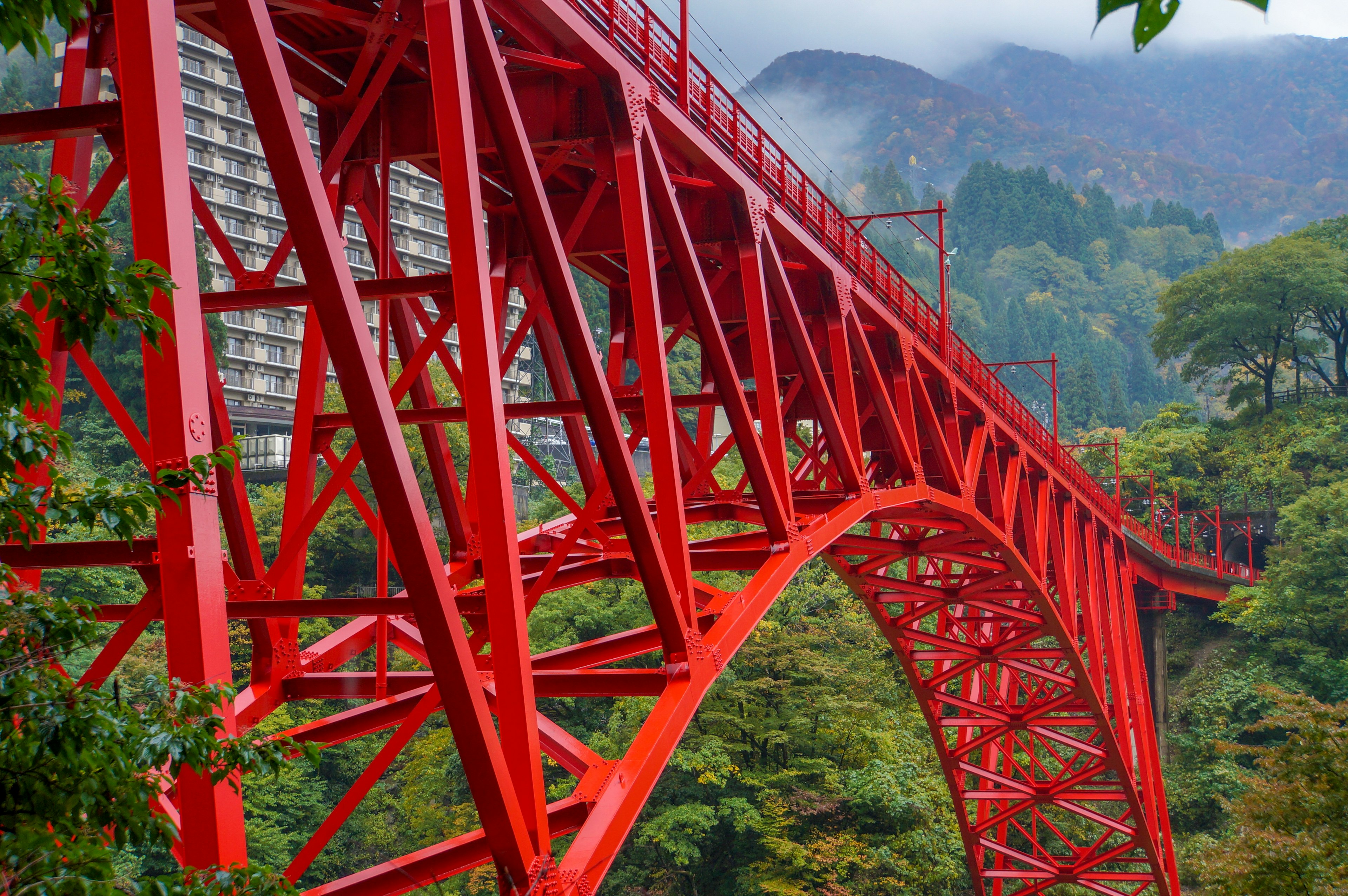 Red steel bridge surrounded by lush mountains