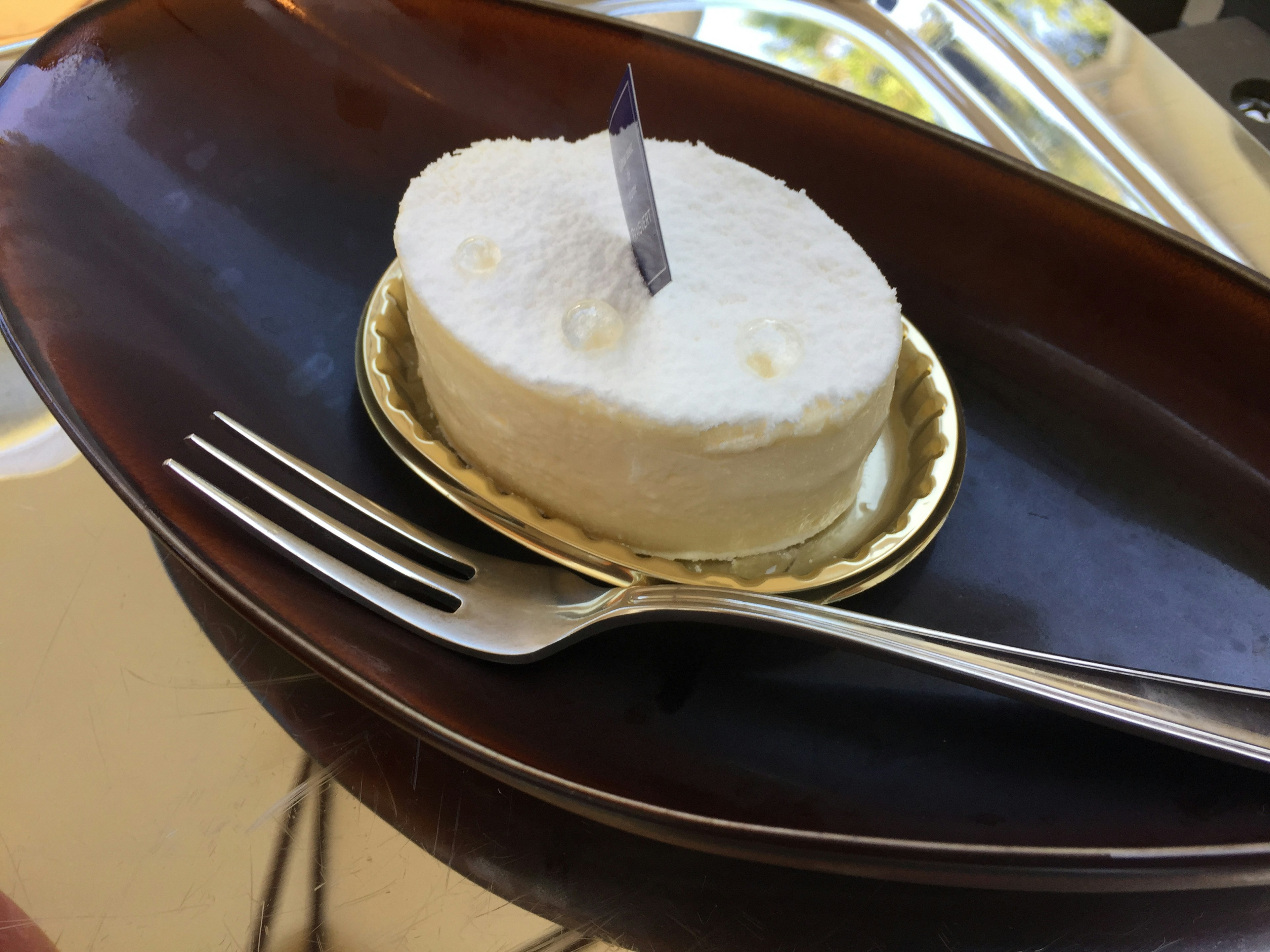 Small white cream cake on a golden plate with a fork beside it