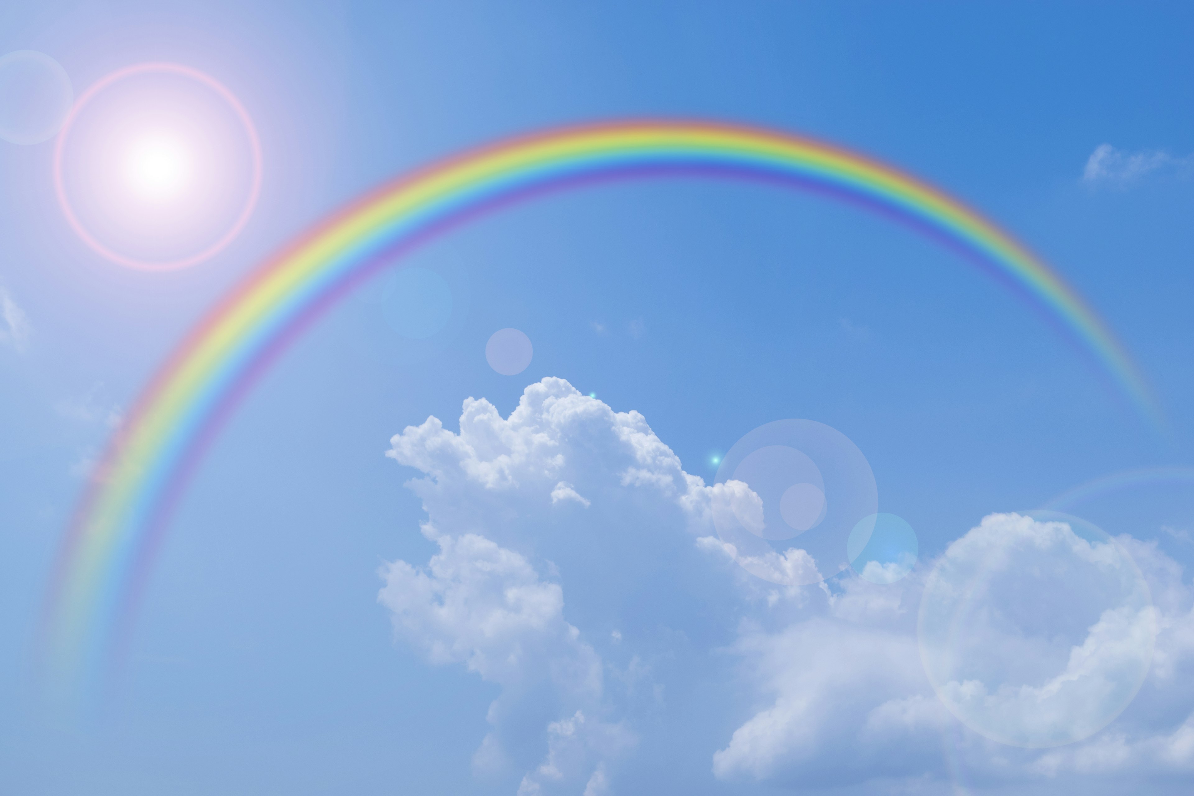 Un arc-en-ciel vibrant dans un ciel bleu avec des nuages blancs duveteux