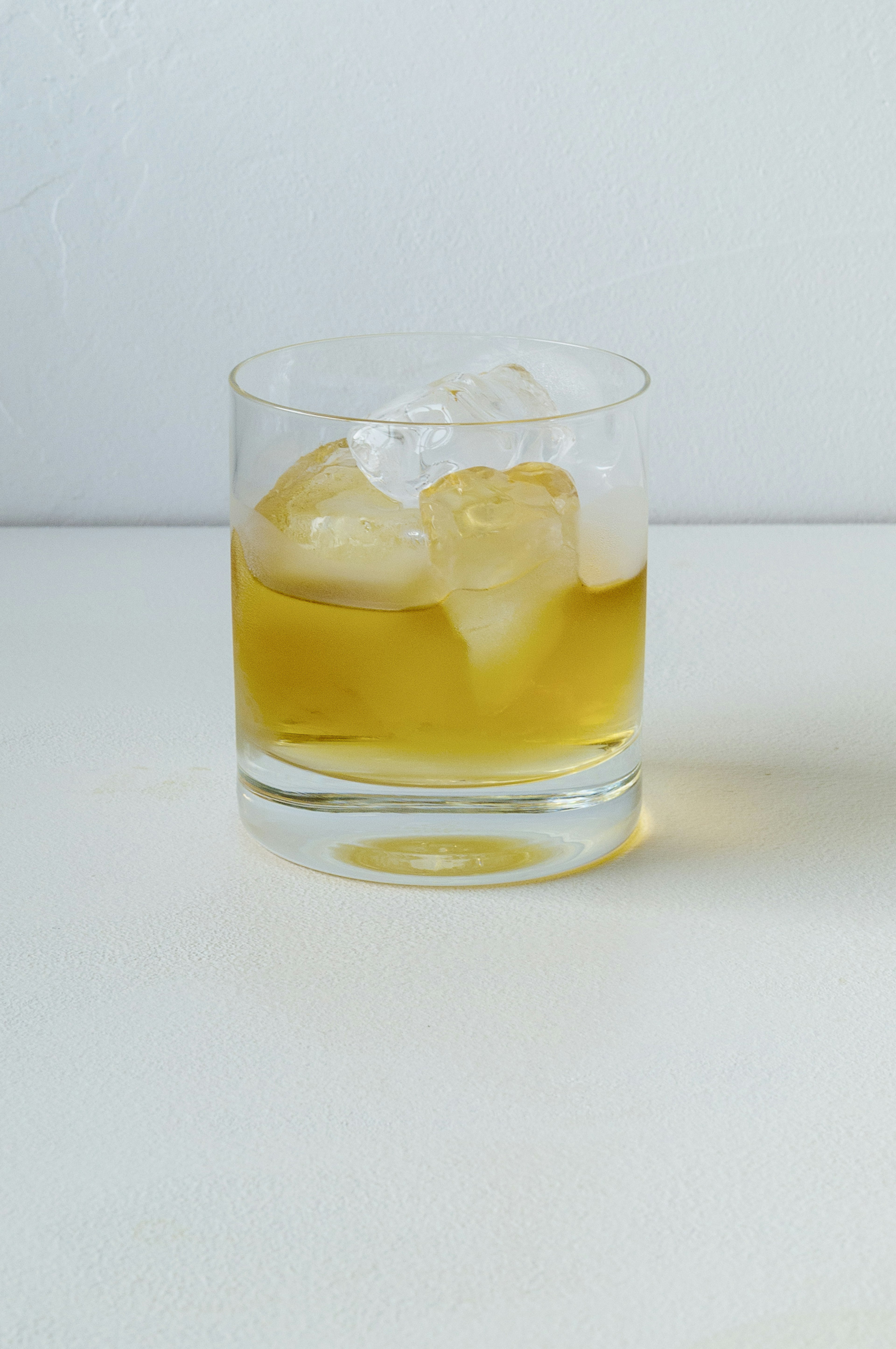 A transparent glass with ice containing a yellow beverage