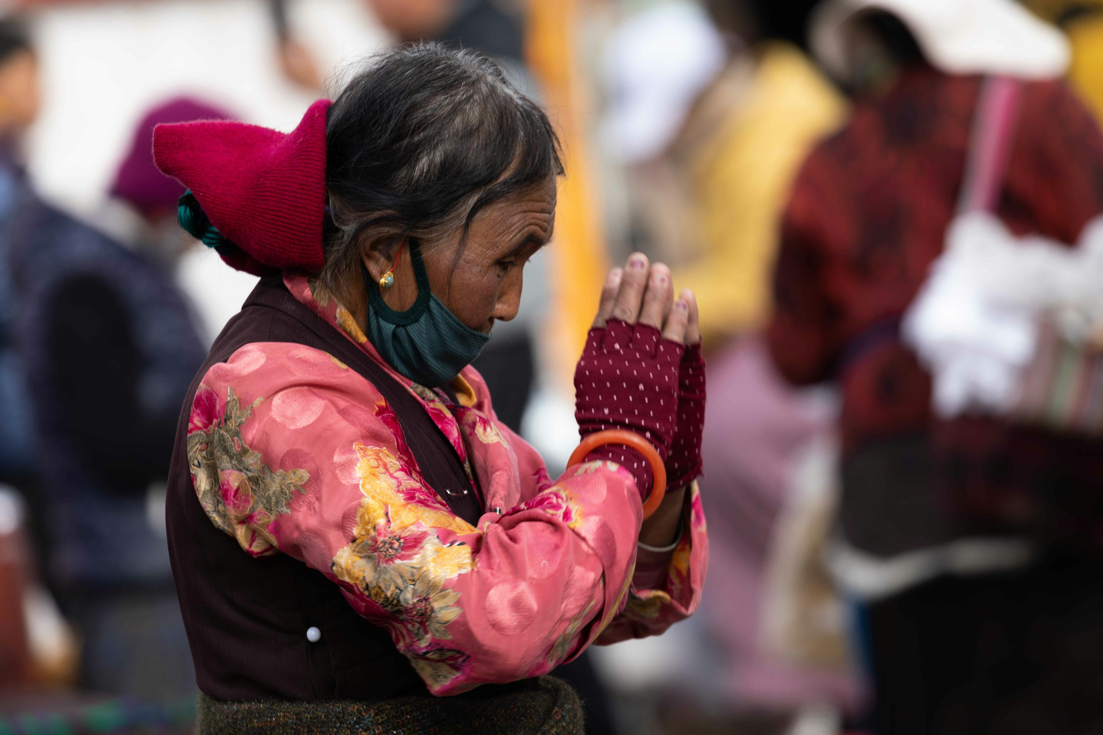 Mujer rezando con atuendo tradicional colorido y mascarilla