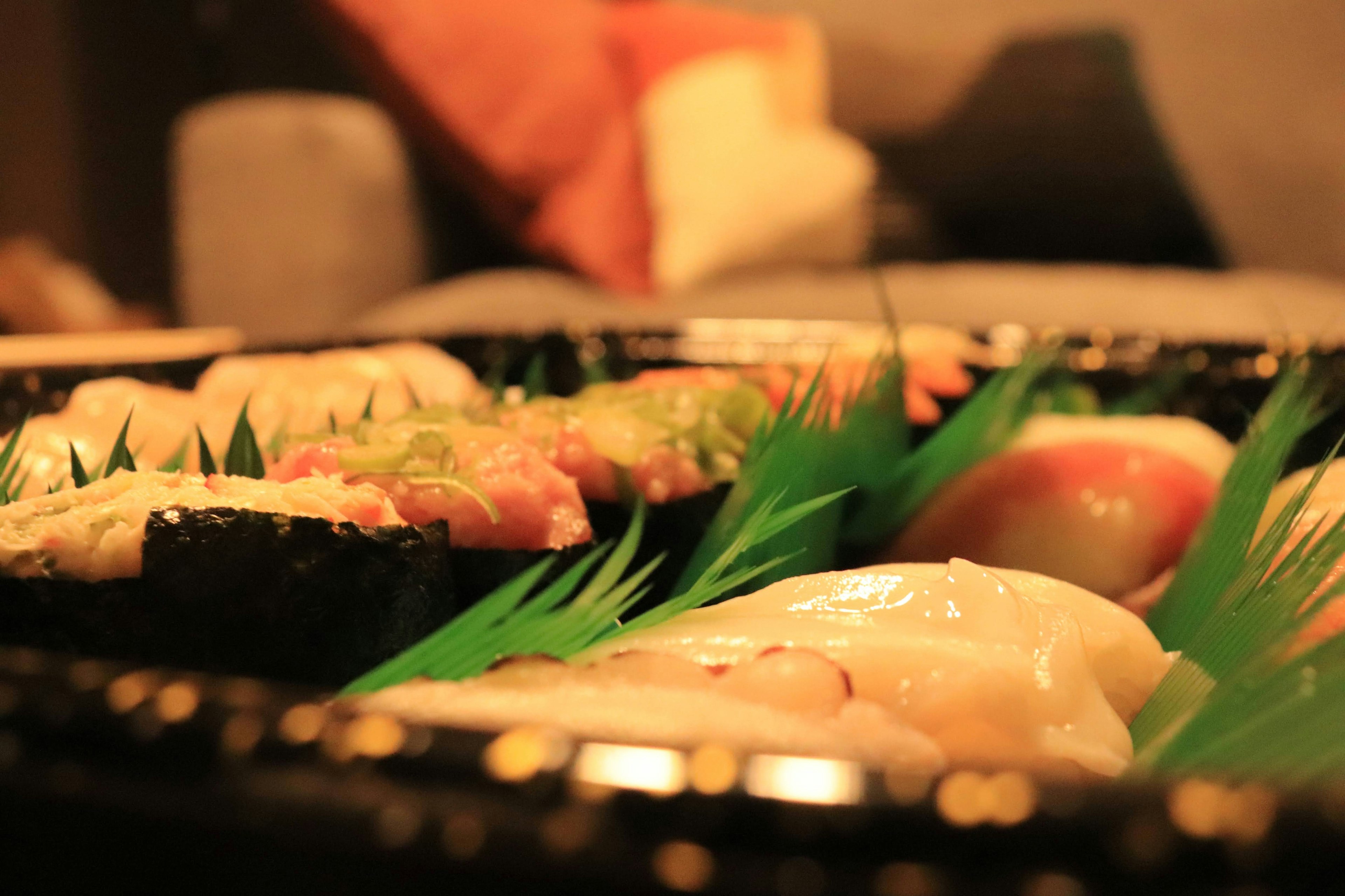 A platter of sushi arranged on green leaves in a cozy setting