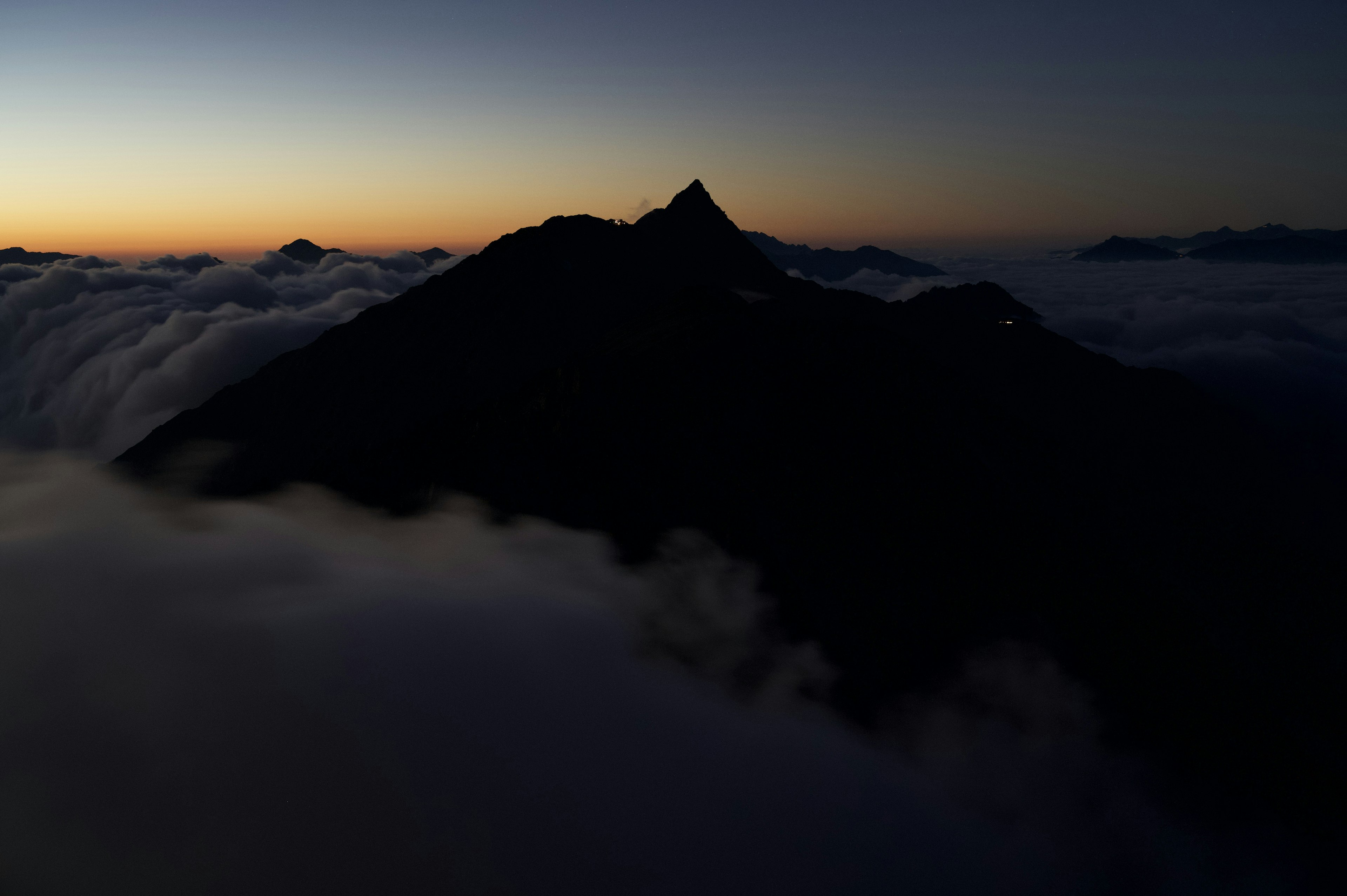 Silhouette eines Berges, der über den Wolken bei Sonnenuntergang aufsteigt