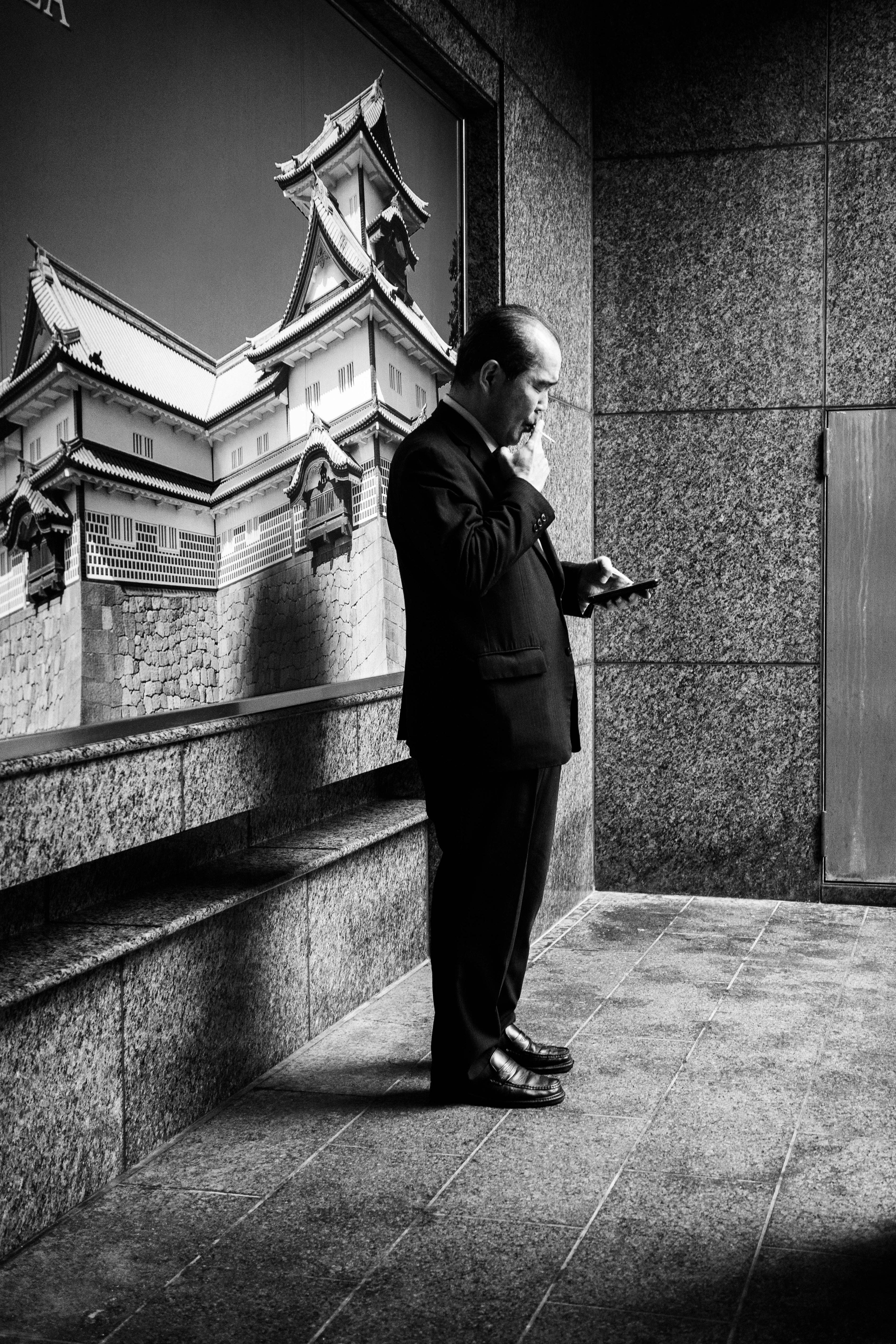 Foto en blanco y negro de un hombre con traje usando un smartphone con un reflejo de arquitectura tradicional en el fondo