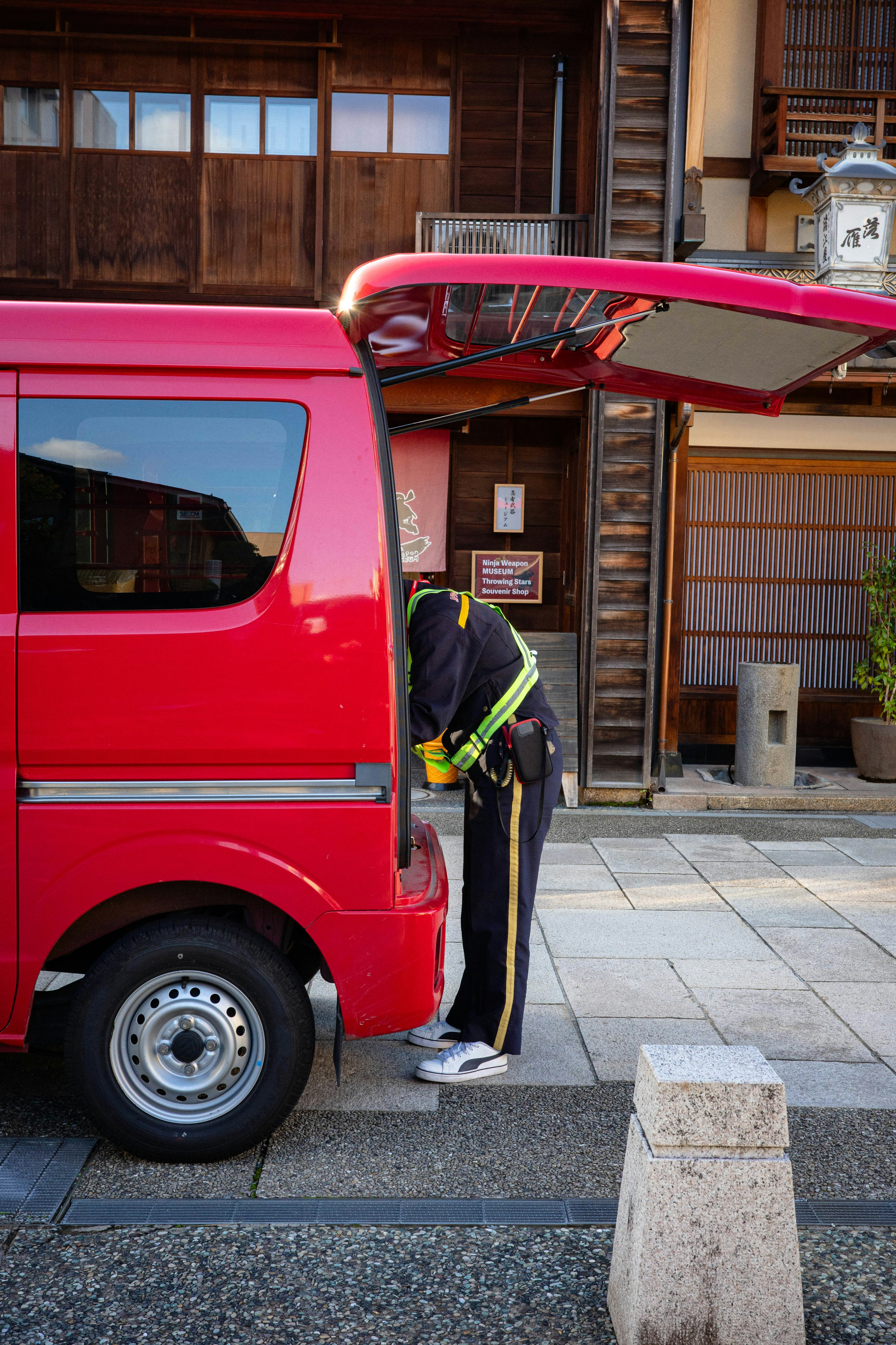 Person, die am Heck eines roten Vans in einer traditionellen Straßenumgebung arbeitet