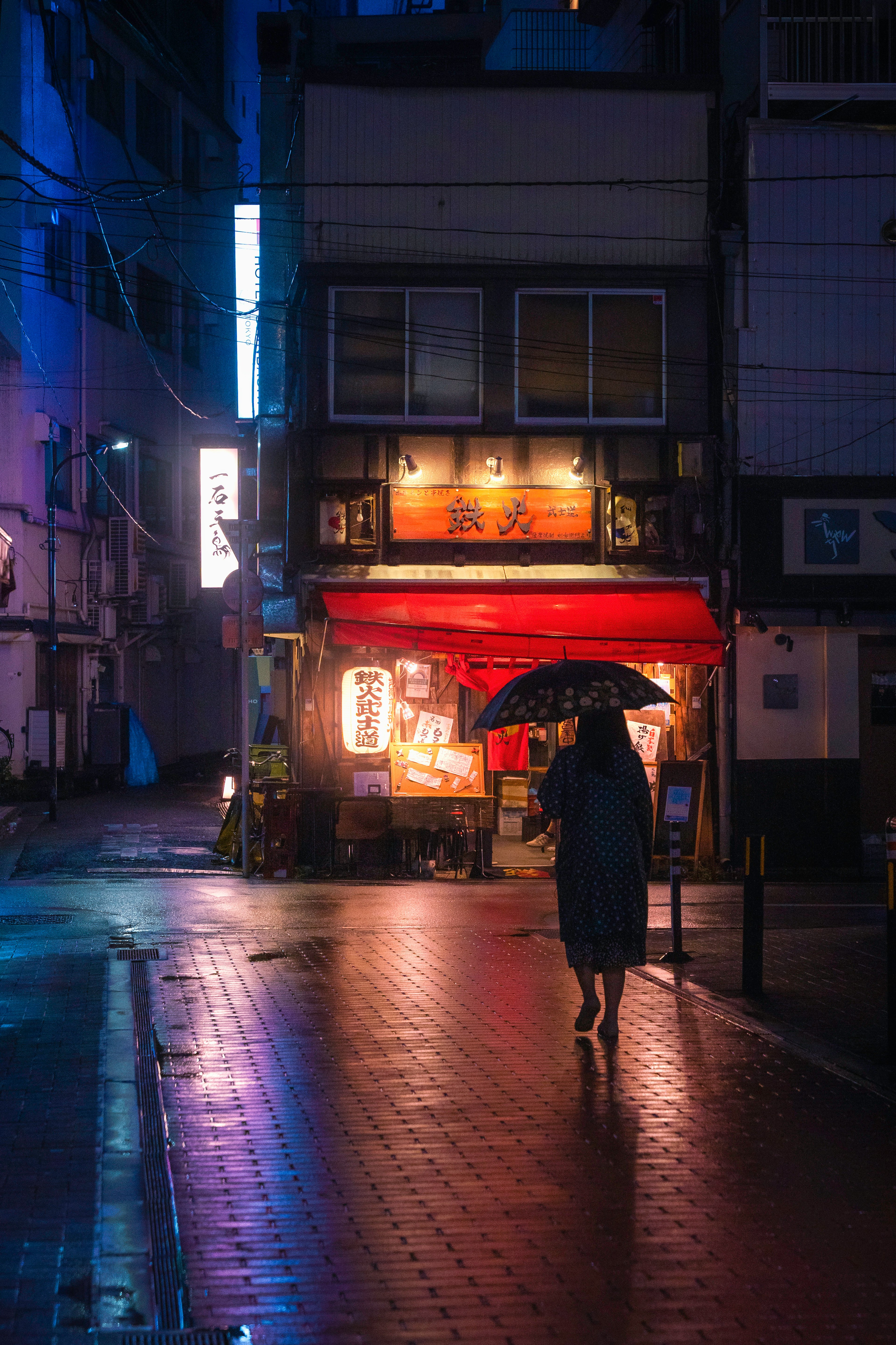 夜の街を歩く傘を持った人とネオンの看板のある店