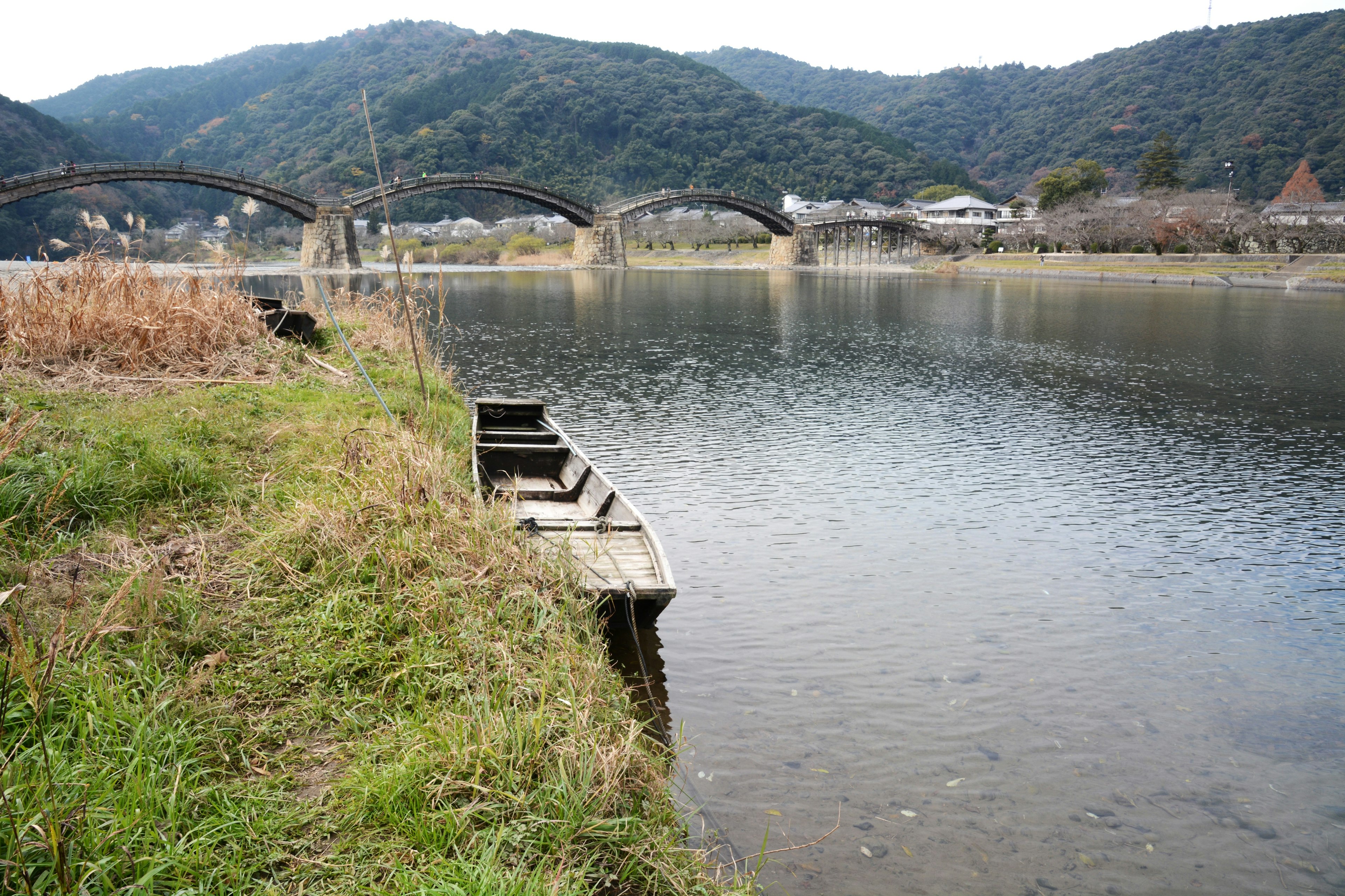 静かな川の風景にかかる橋と草の生えた岸辺の小舟