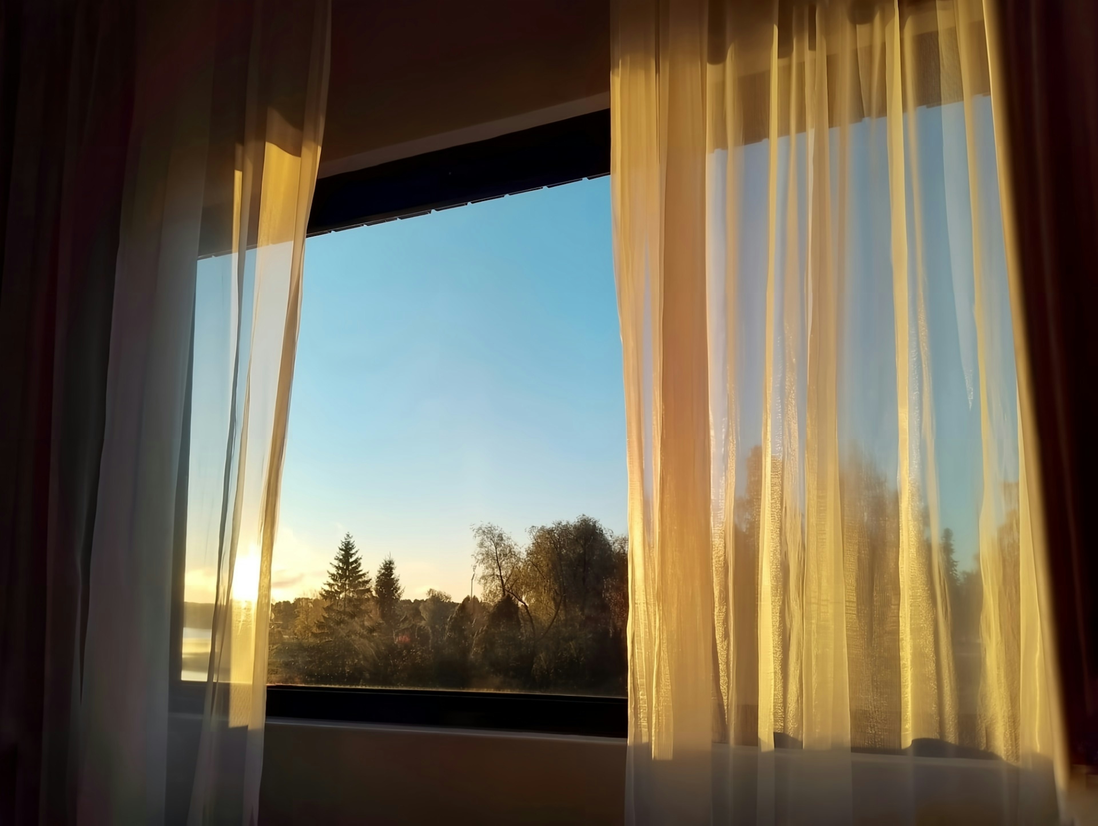 Blick auf den Sonnenuntergang durch transparente Vorhänge in einem Fenster