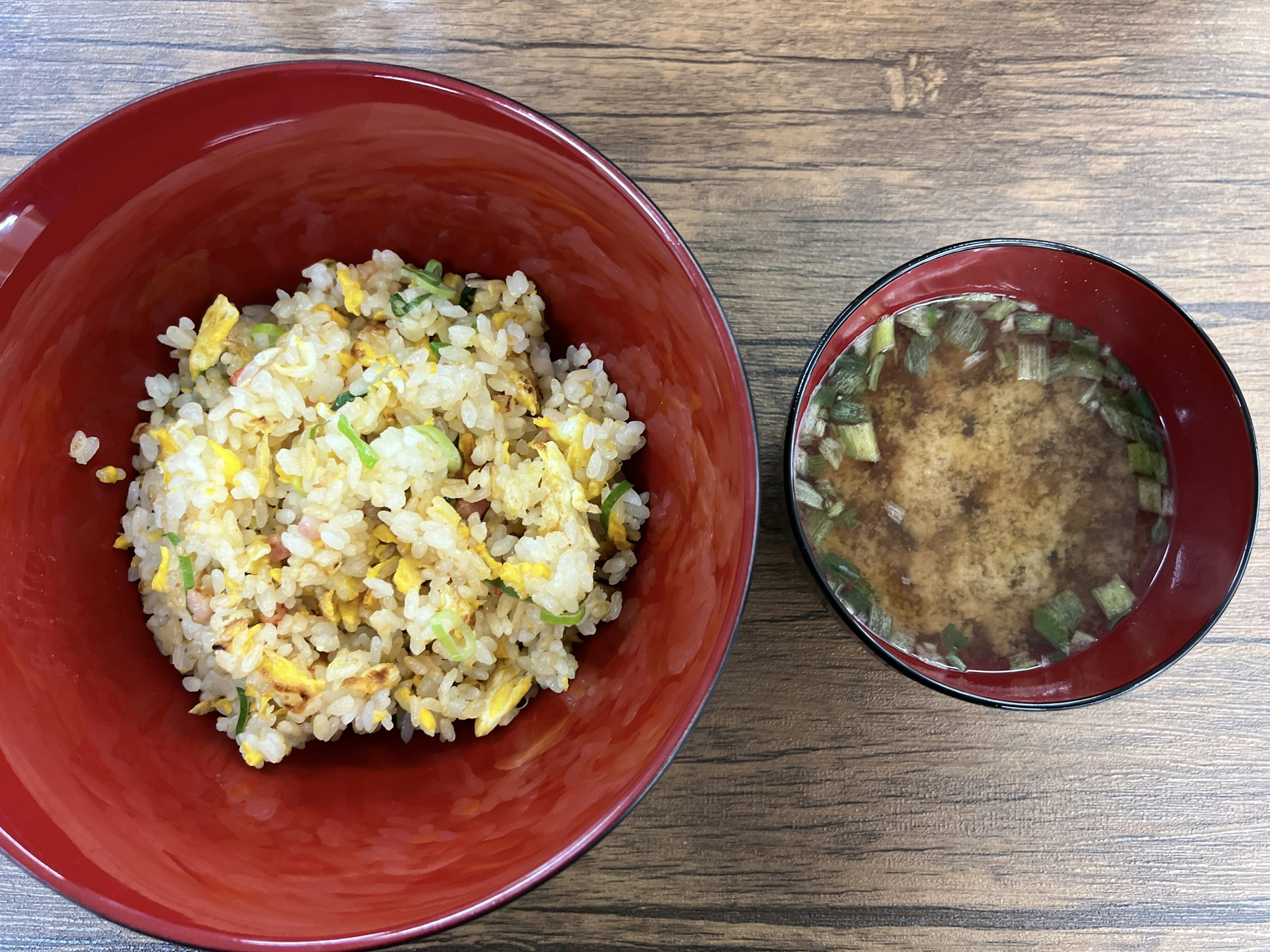 Fried rice served in a red bowl alongside a cup of soup