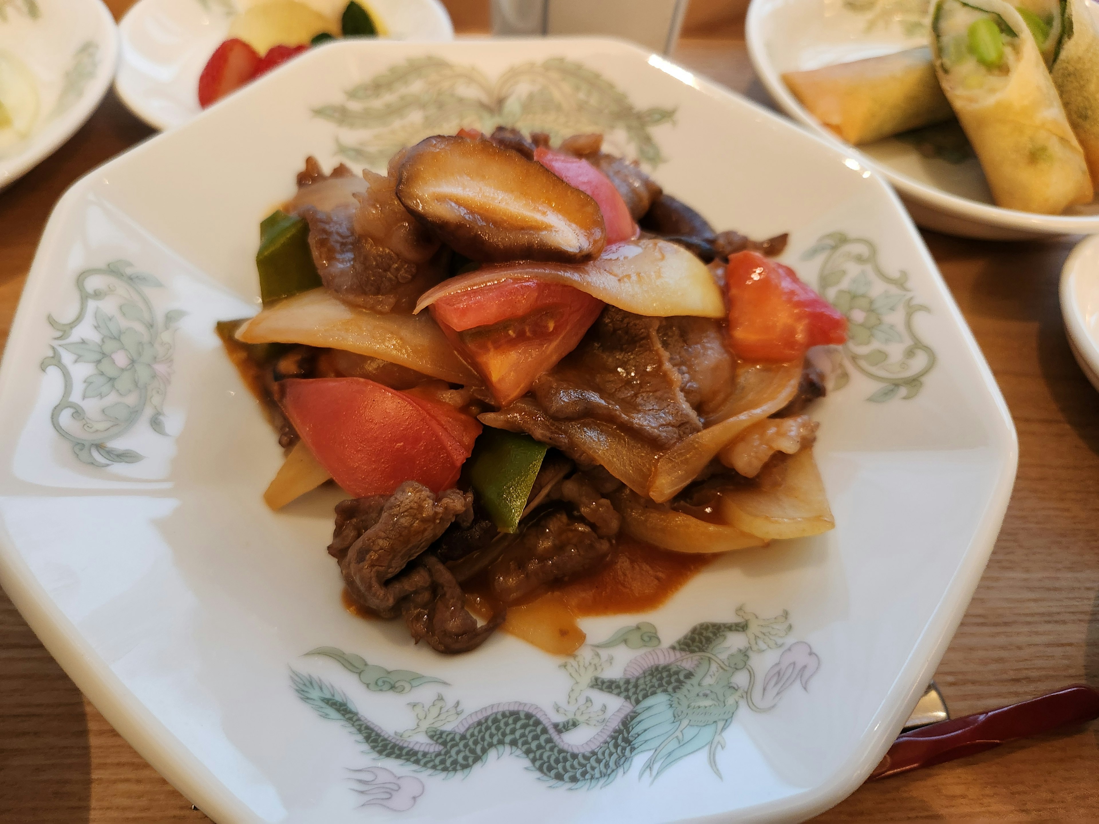 Un plato colorido de carne y verduras servido en un plato blanco con tomates y pimientos