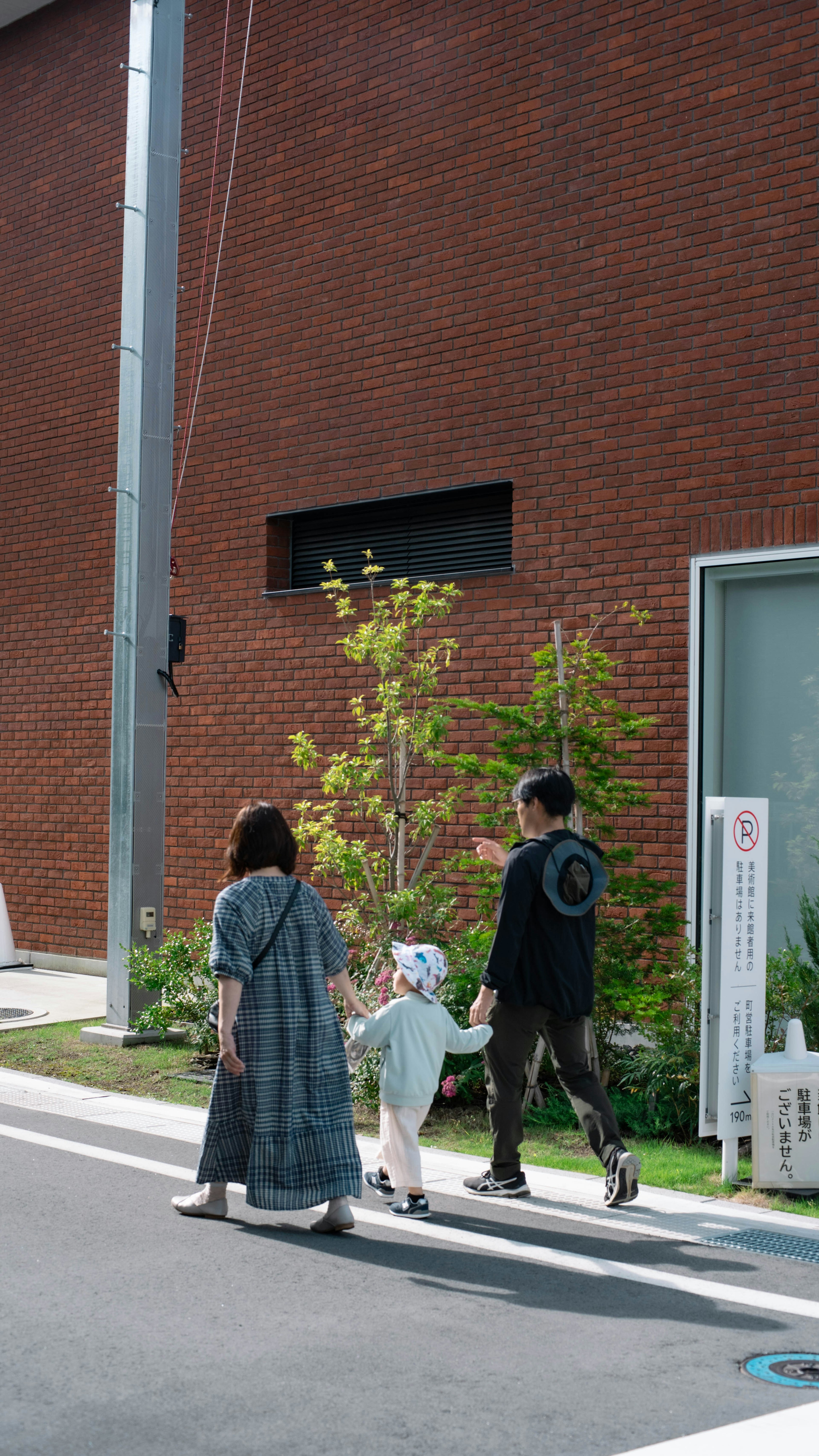 家族が手をつなぎながら歩いているシーン 緑の植物とレンガの壁が背景