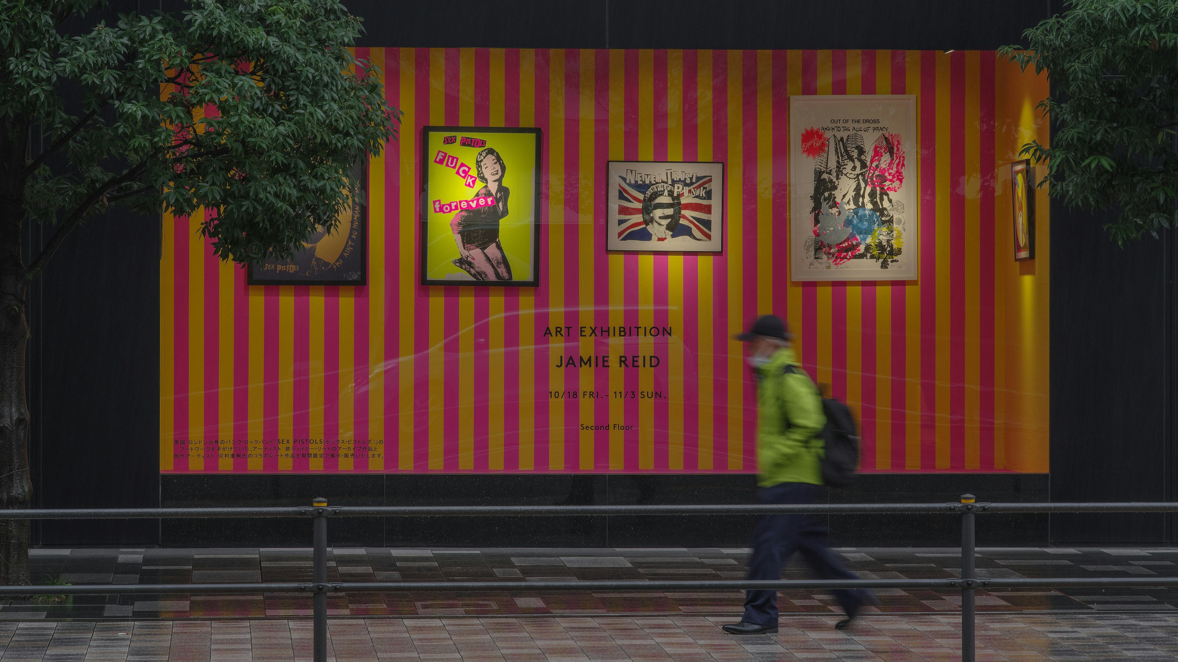 Una persona che cammina sotto la pioggia con opere d'arte su un muro a strisce colorate sullo sfondo