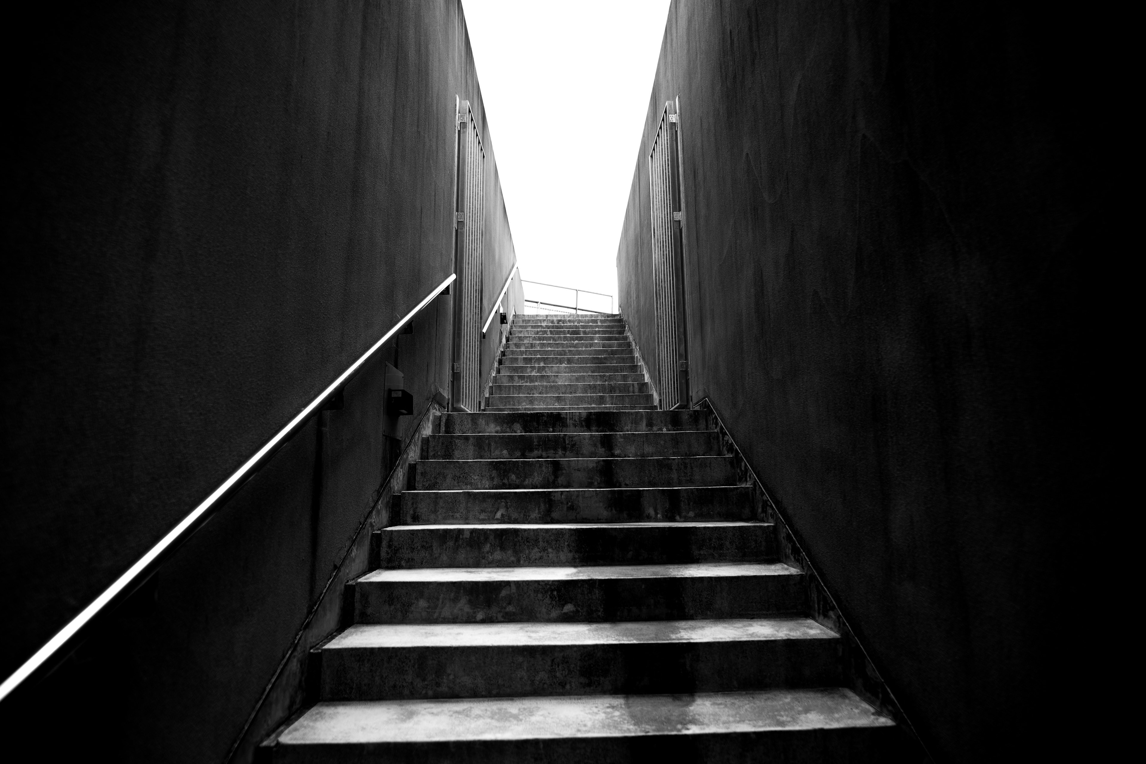 Foto en blanco y negro de escaleras que llevan hacia arriba luz brillante que proviene de arriba