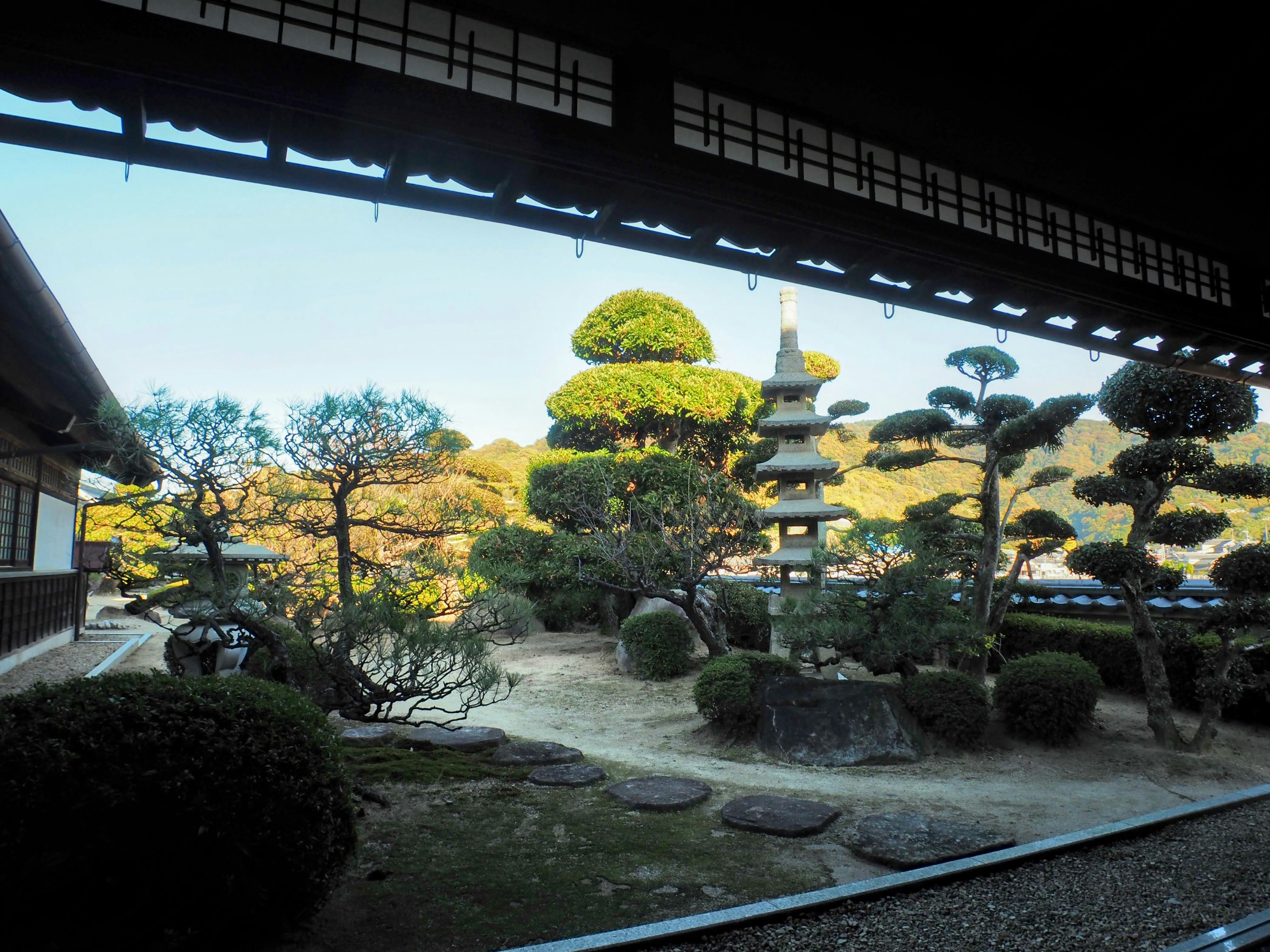 Vista di una casa giapponese tradizionale che si affaccia su un giardino con bellissimi pini e una pagoda in pietra