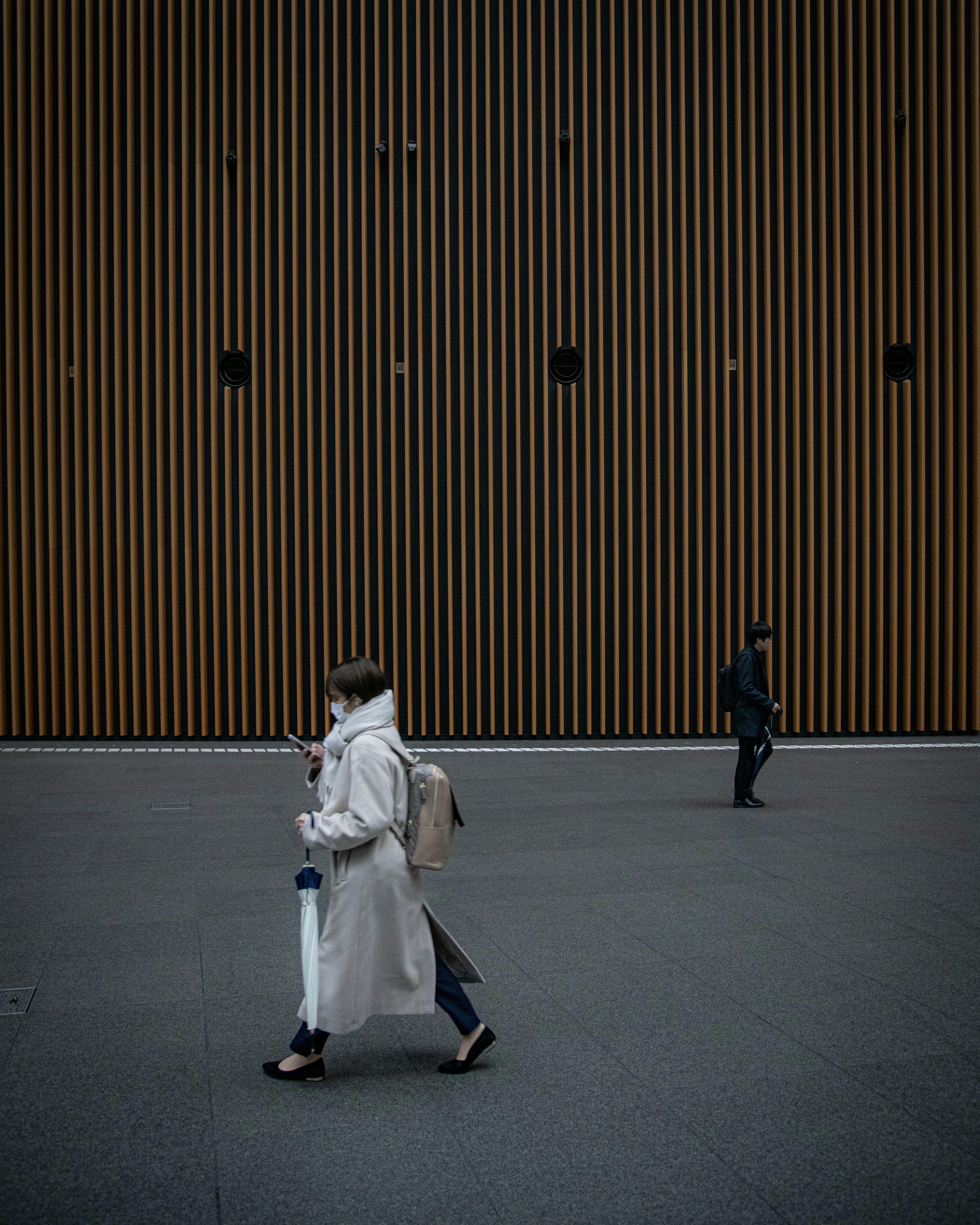 A woman in a white coat walking against a wooden striped wall