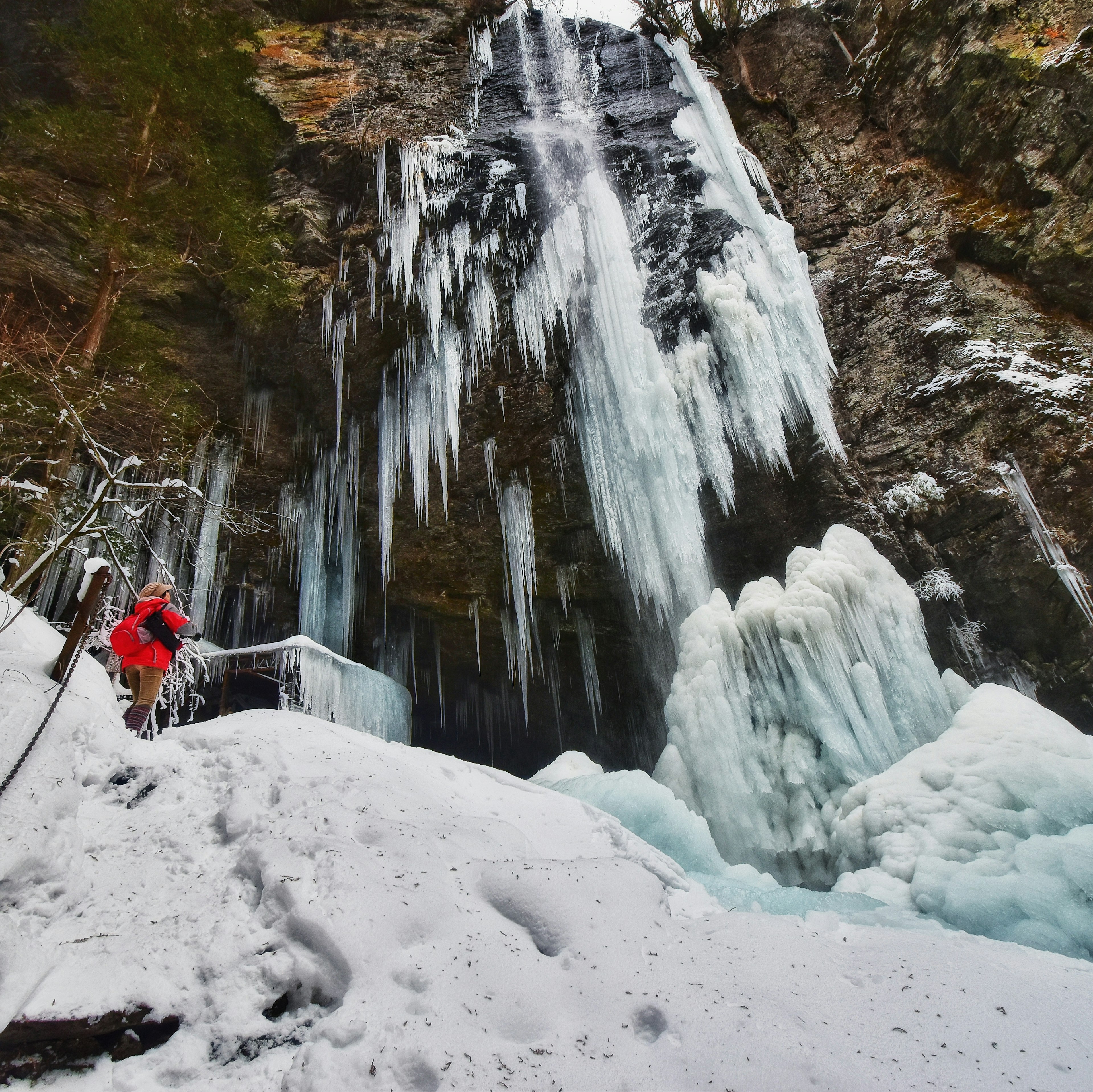 Un grimpeur en veste rouge se tient devant une cascade glacée entourée de neige