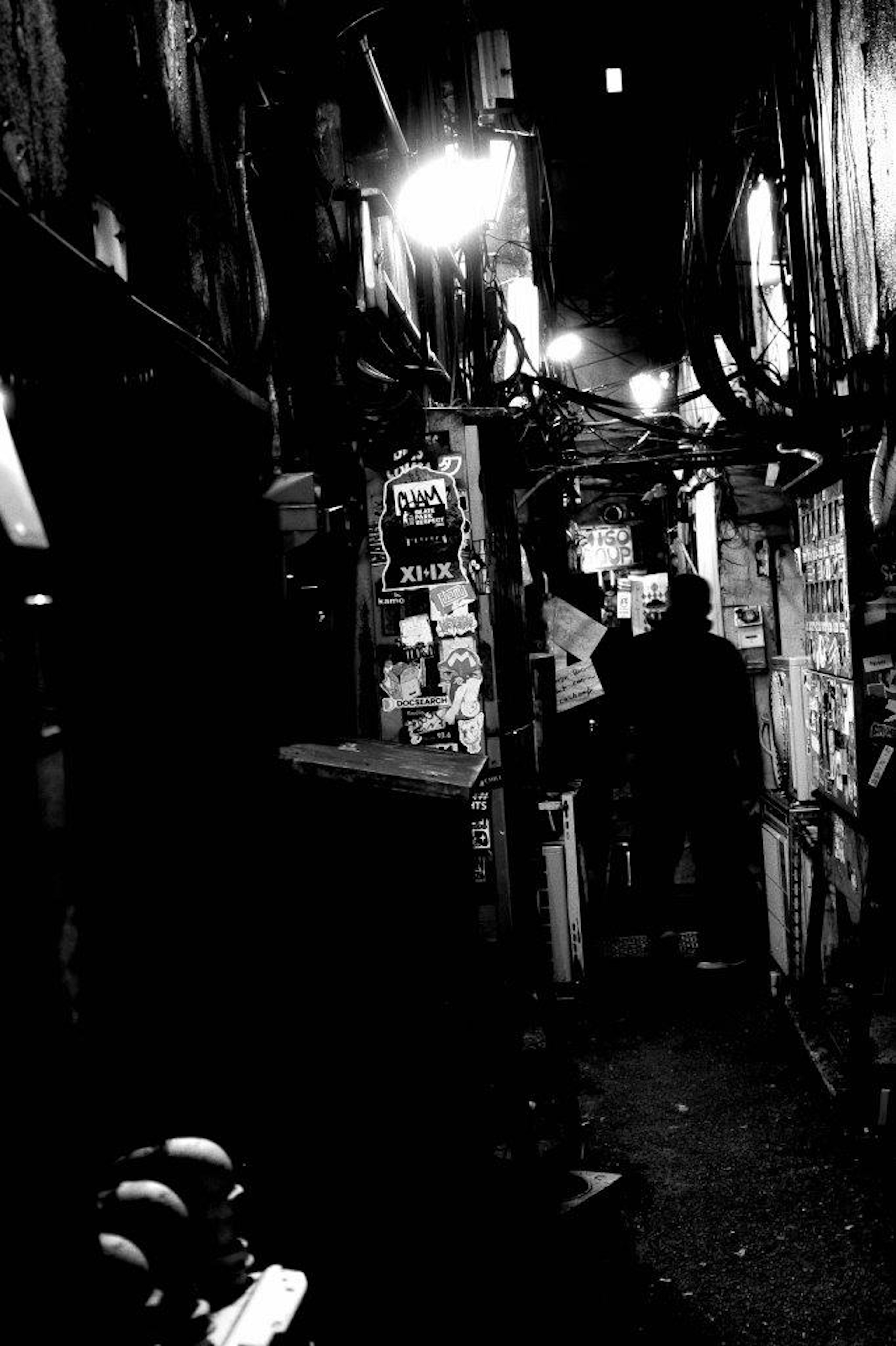 A monochrome photo of a figure standing in a dim alley with streetlights