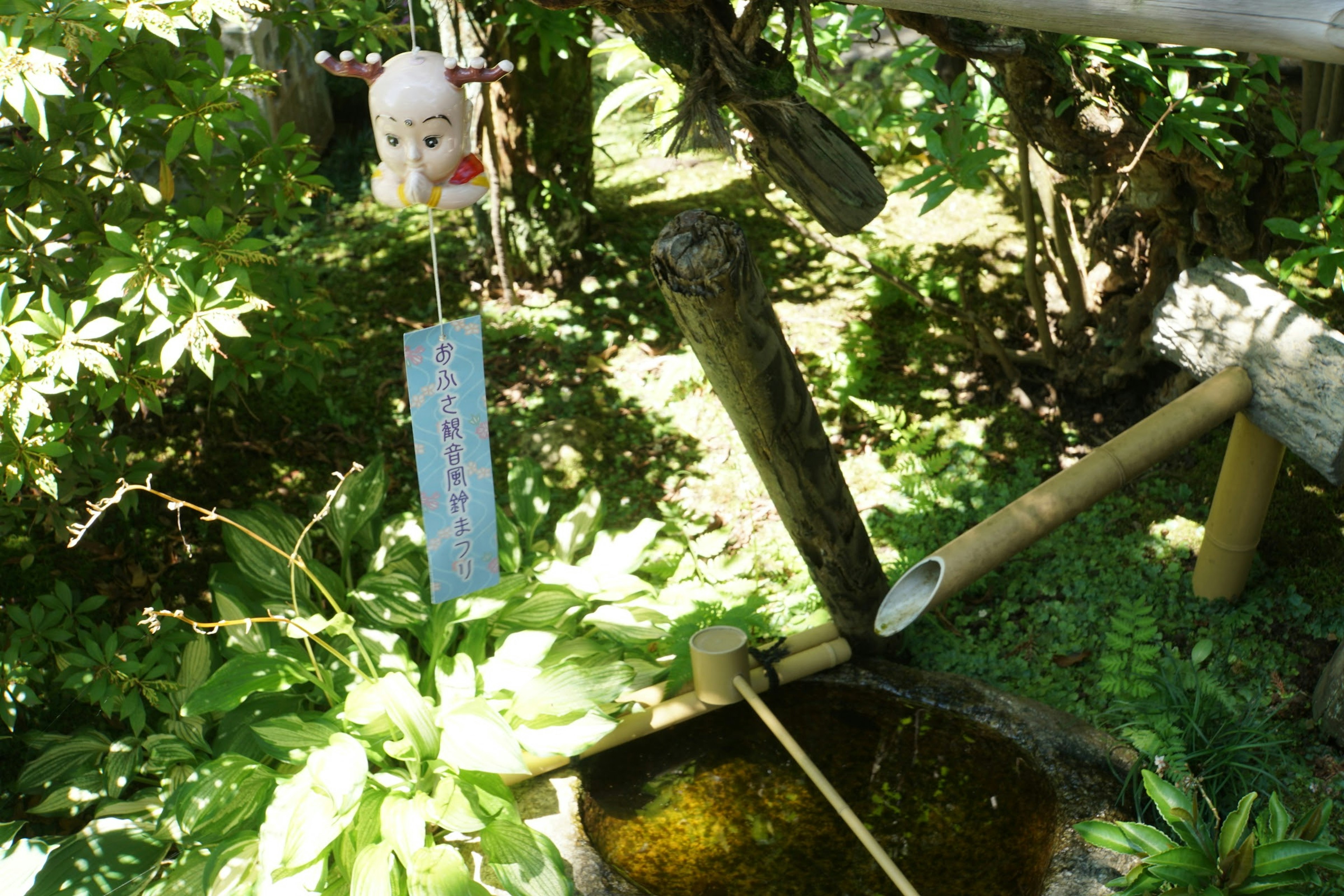 Japanischer Garten mit Bambus-Wassermerkmal und üppigem Grün mit einem hängenden Windspiel