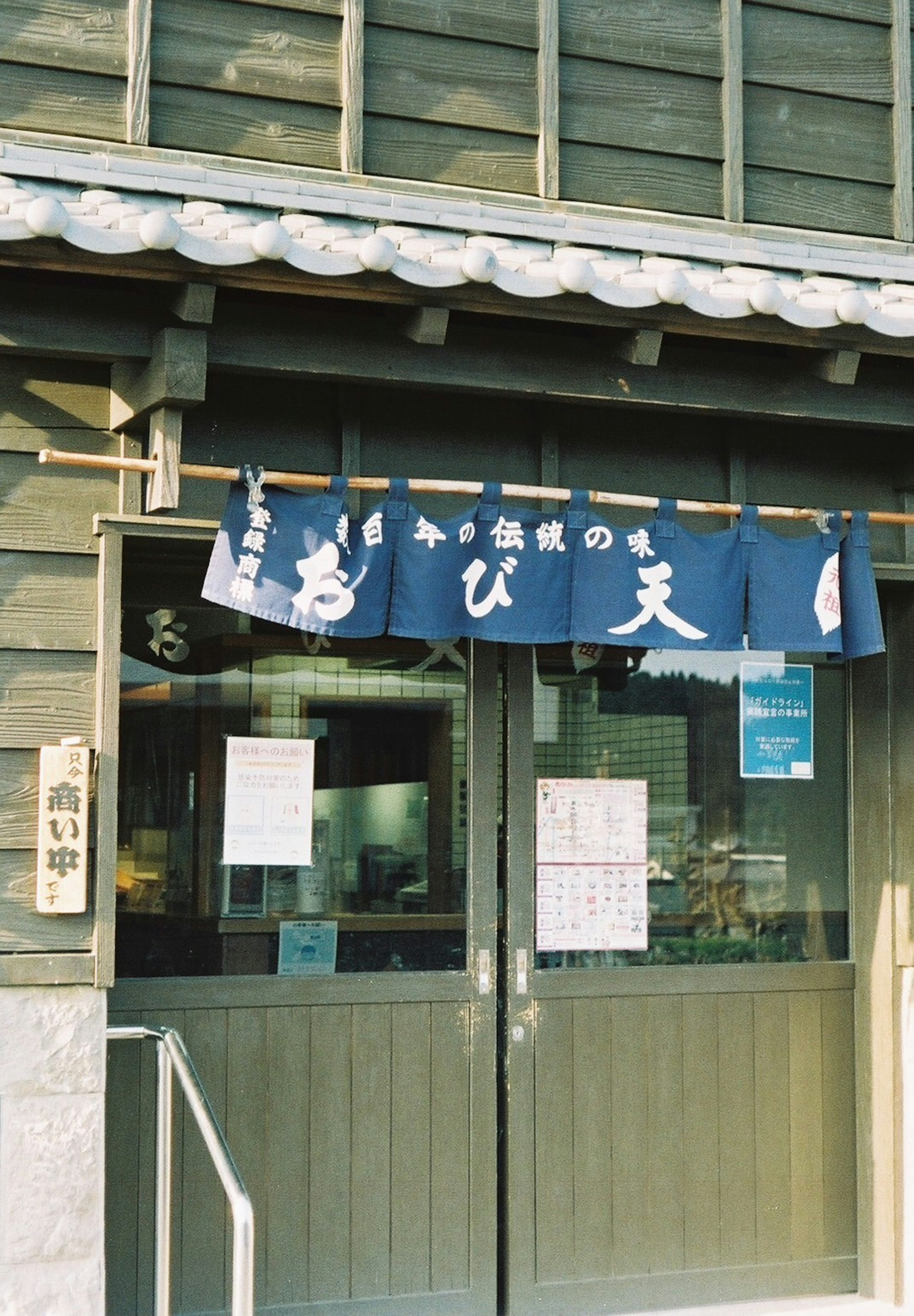 古い日本の建物の外観に青い暖簾が掛かる店舗の入り口