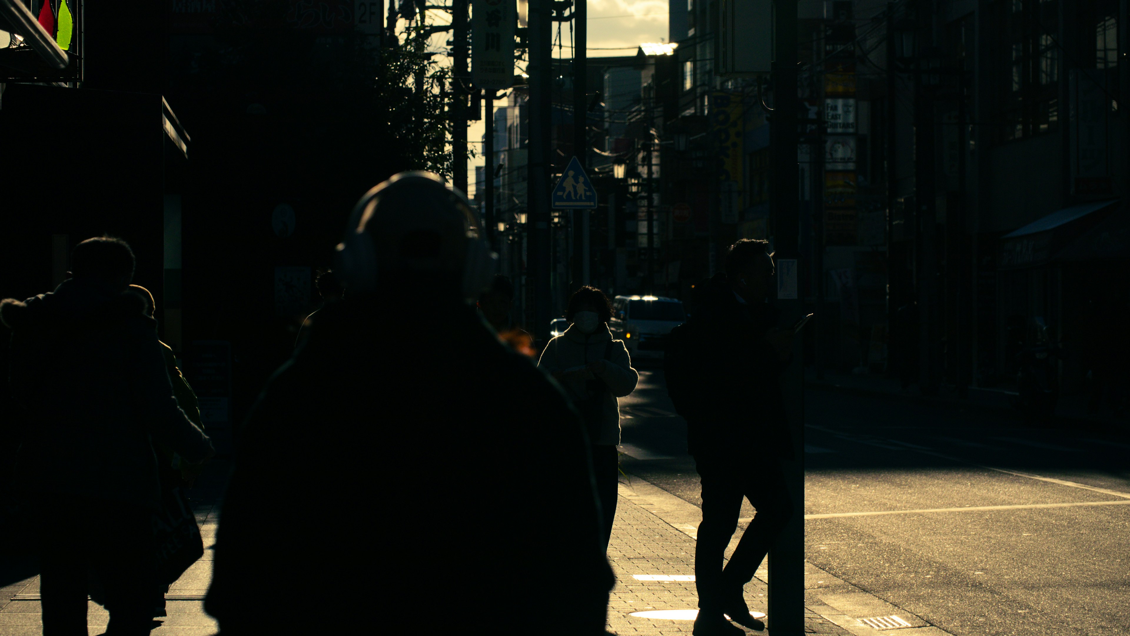 Figuras en silueta cruzando una calle con luz de atardecer