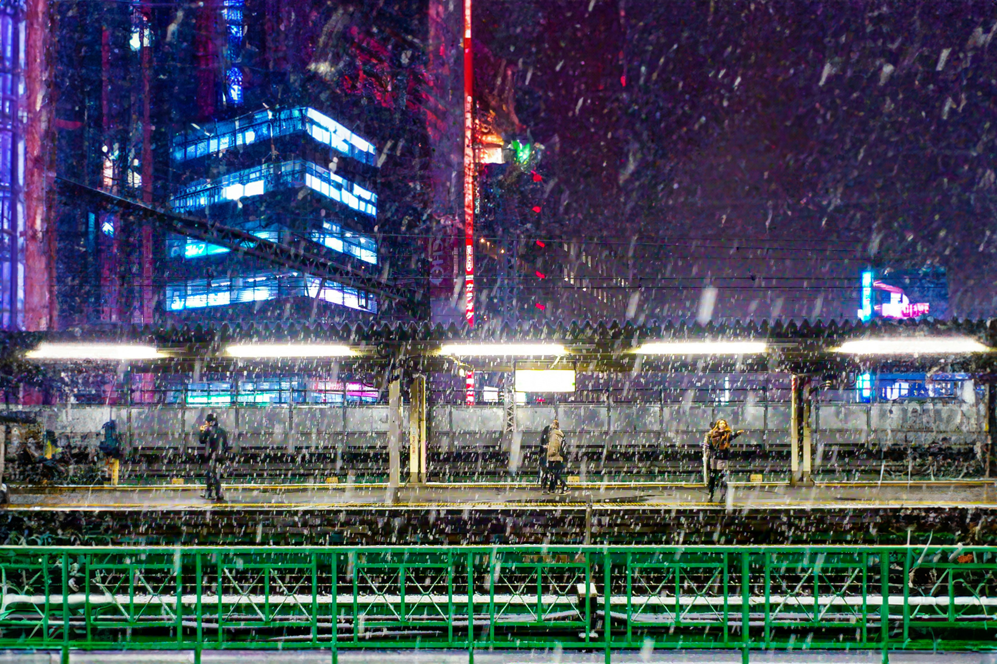 Snowy night cityscape featuring a train platform and illuminated buildings