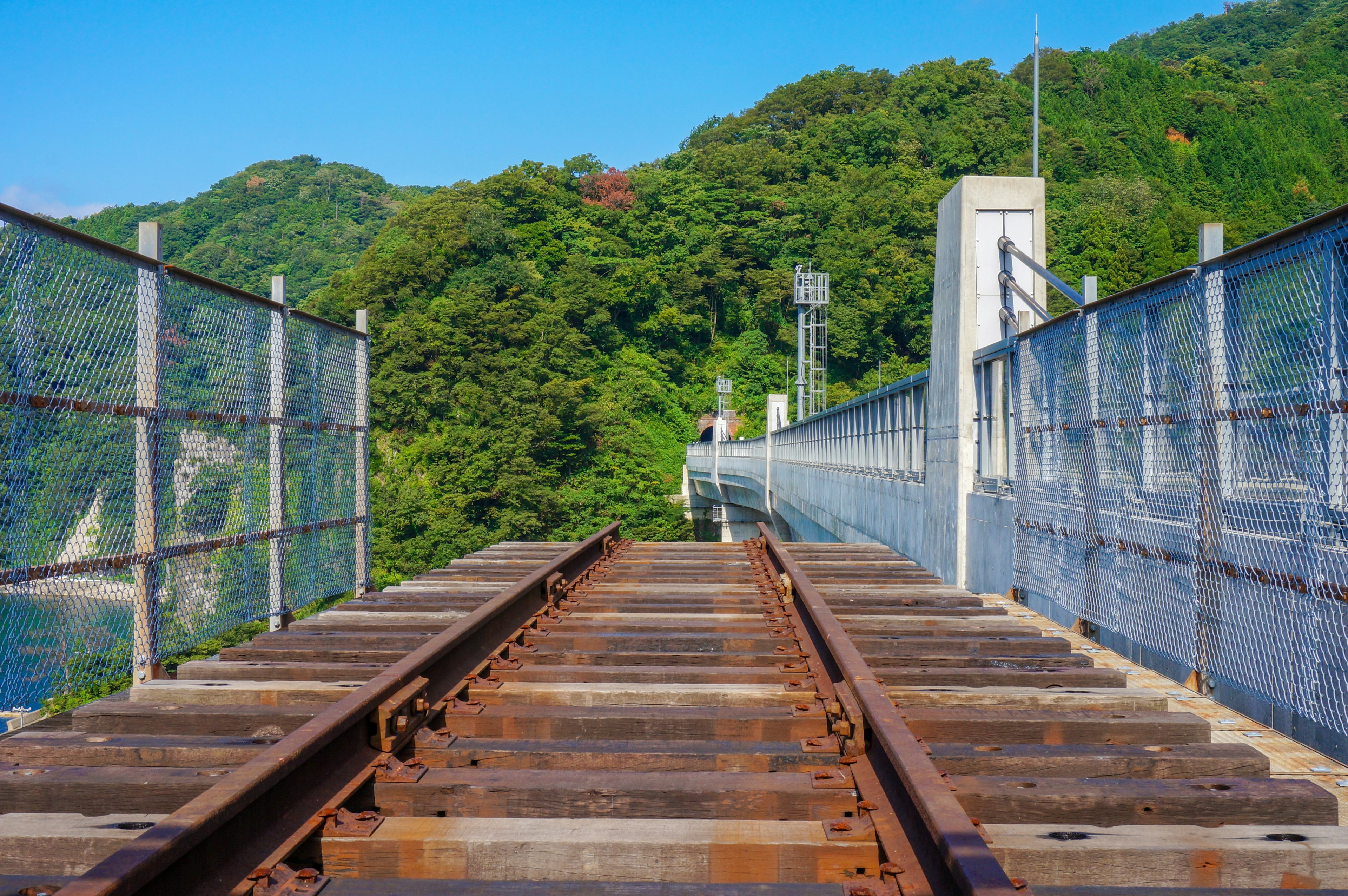 View of railway tracks with a fence surrounded by green hills