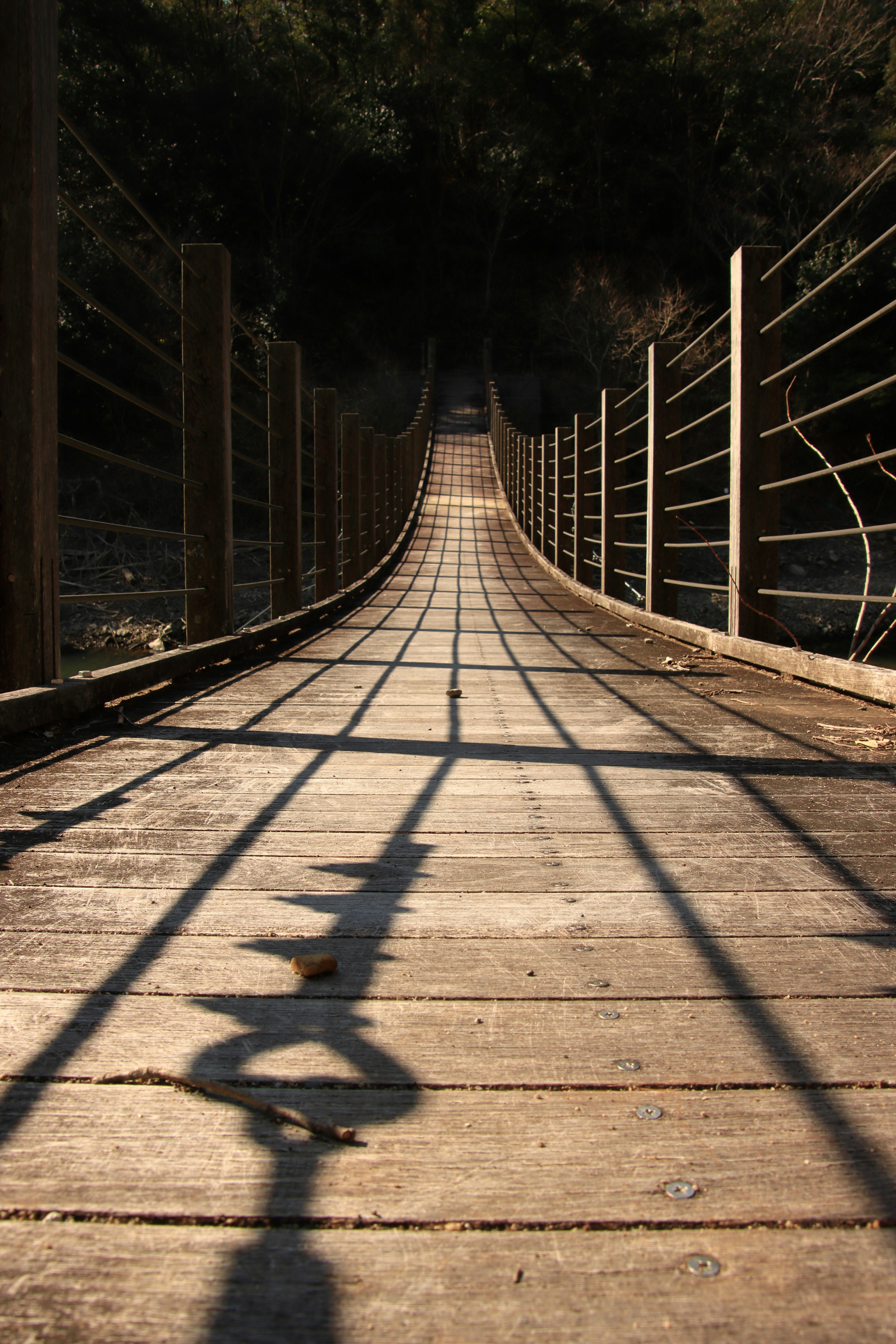 Vista en perspectiva de un puente colgante de madera con patrones de sombra