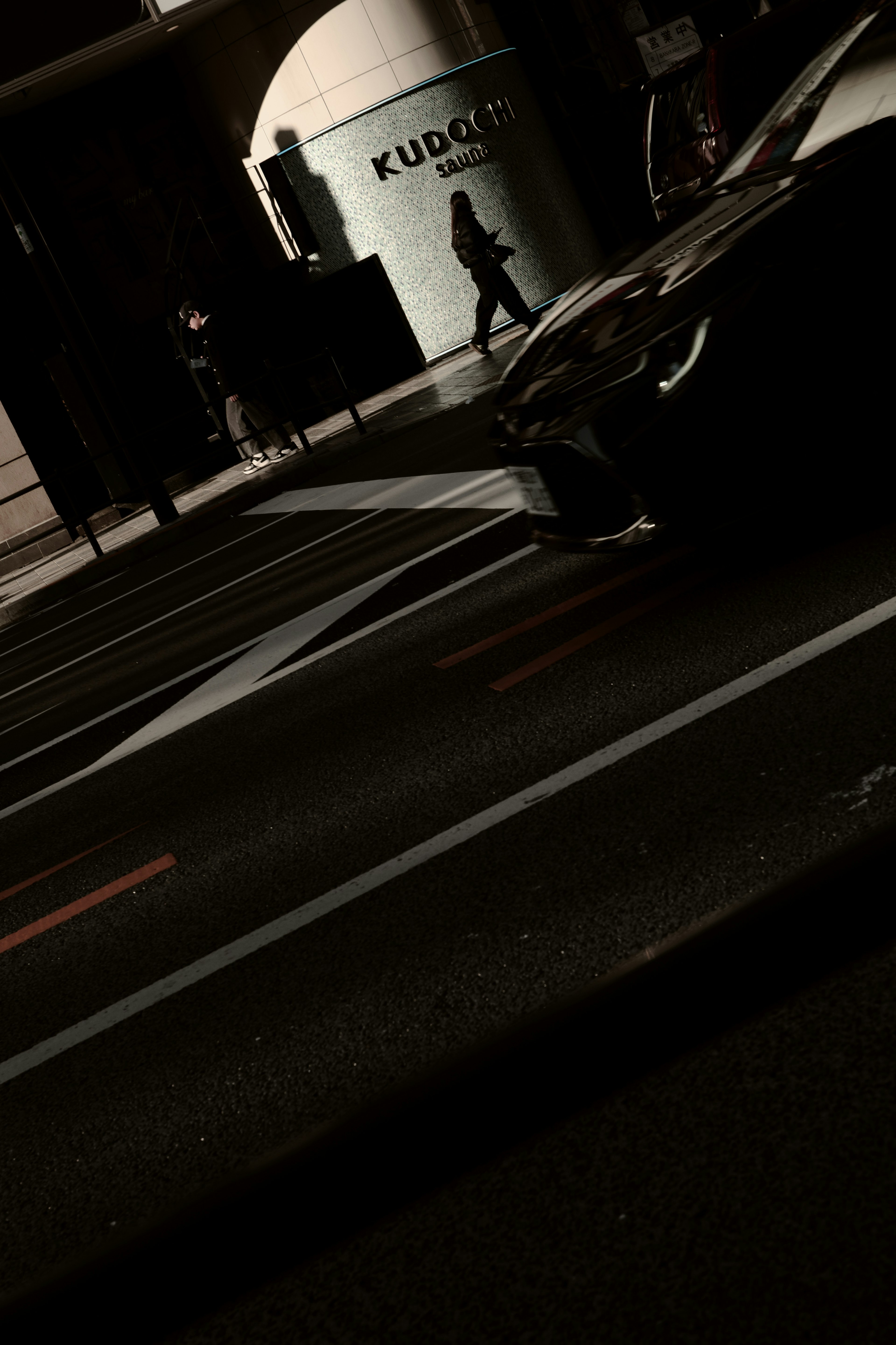 A black car passing by a crosswalk in an urban setting with a silhouette of a person