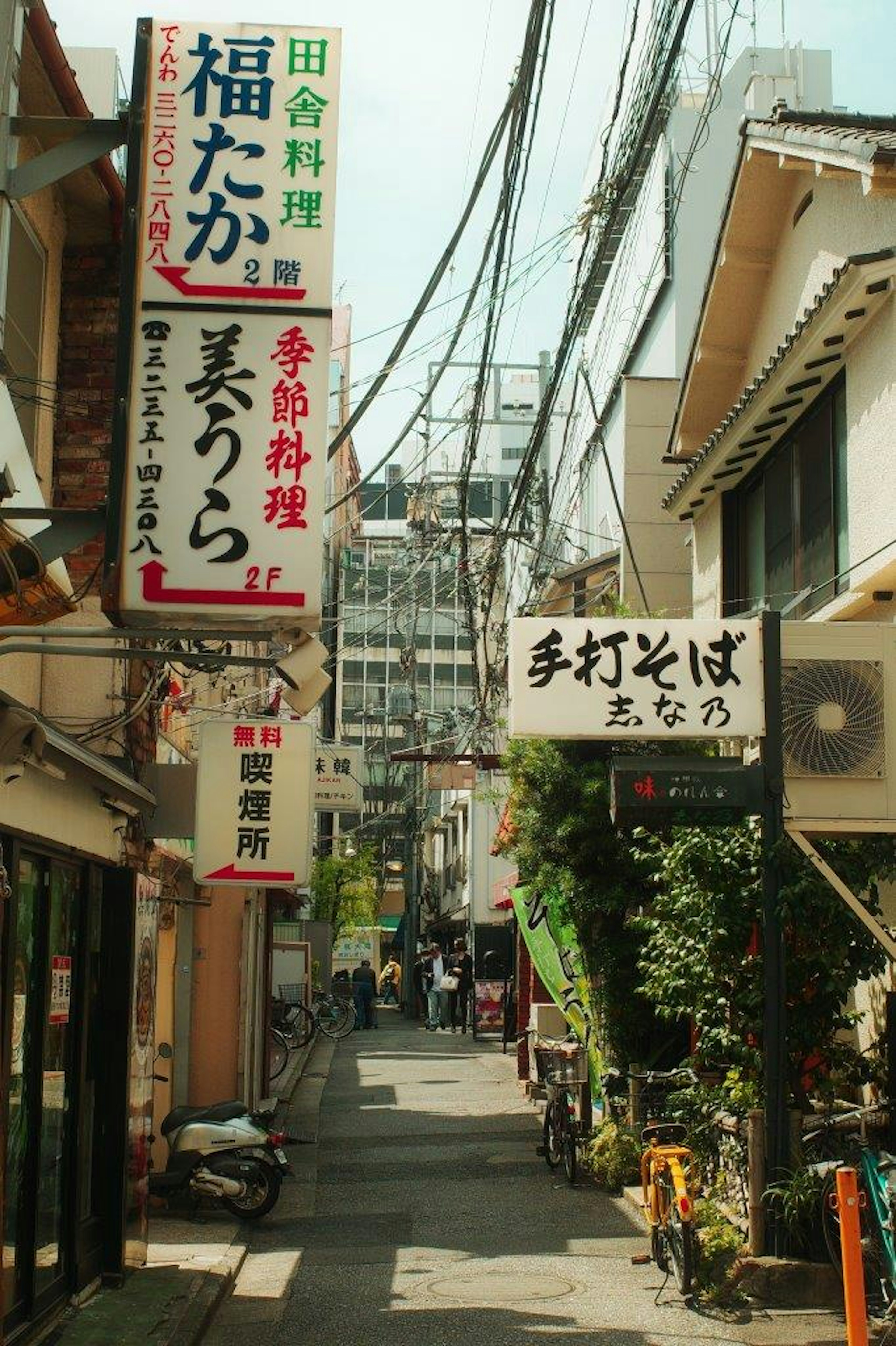 Callejón estrecho con letreros de restaurantes japoneses y cables aéreos