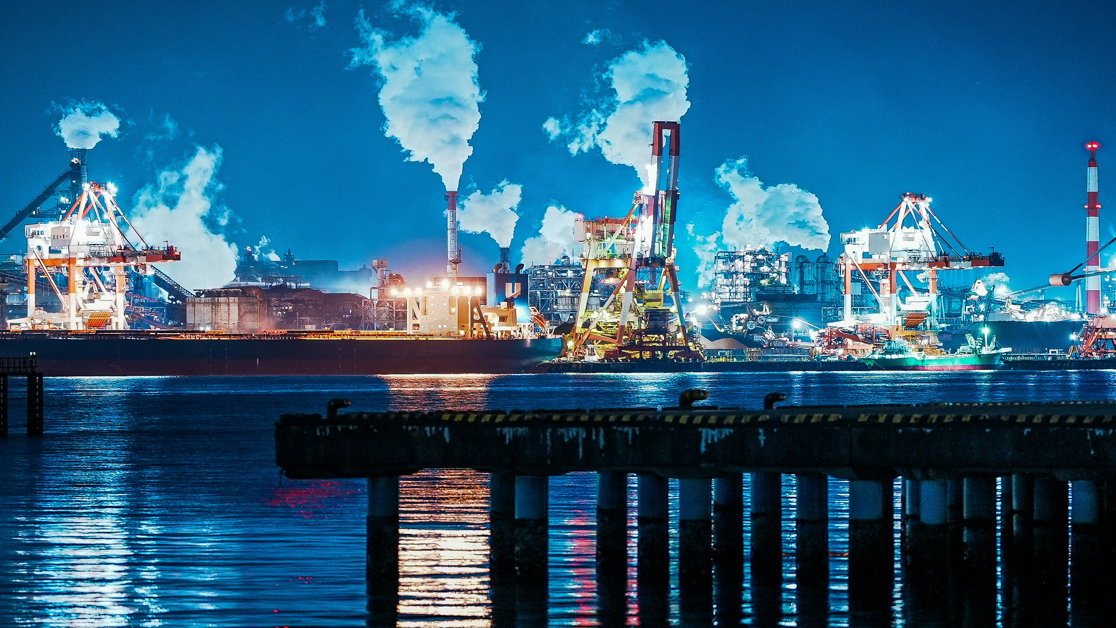 Port industriel de nuit avec des navires et des cheminées émettant de la fumée