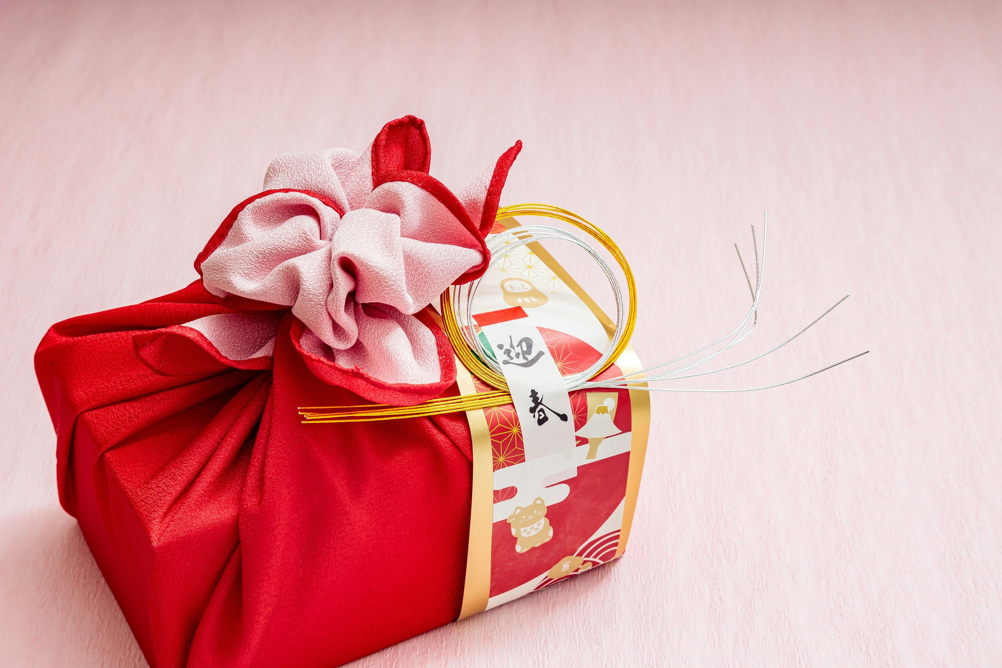 Un cadeau rouge enveloppé avec un ruban rose et orné d'une corde dorée