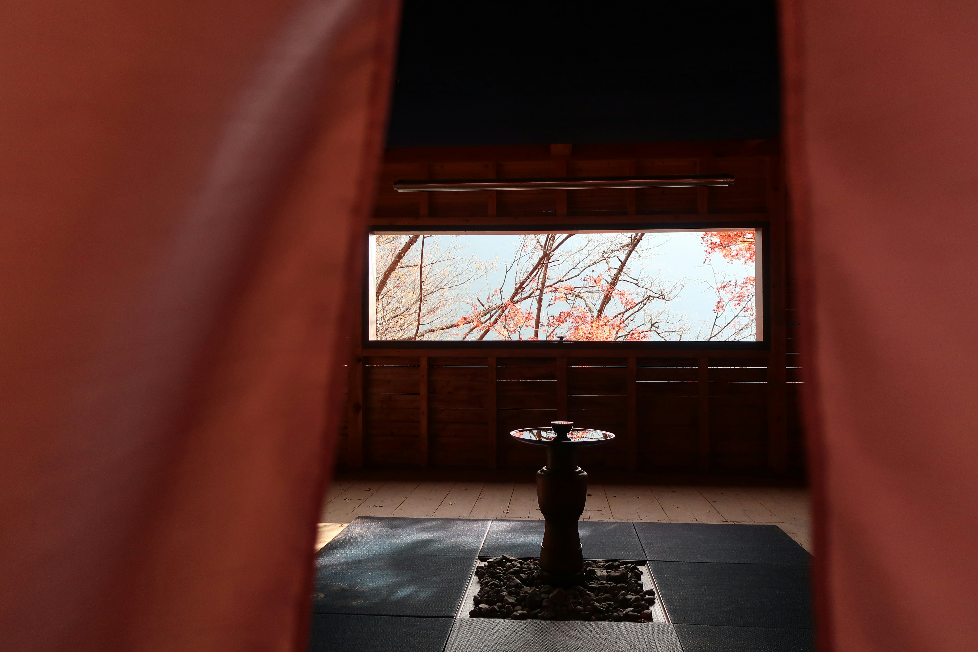 View through red curtains revealing a Japanese room with a window and a water basin