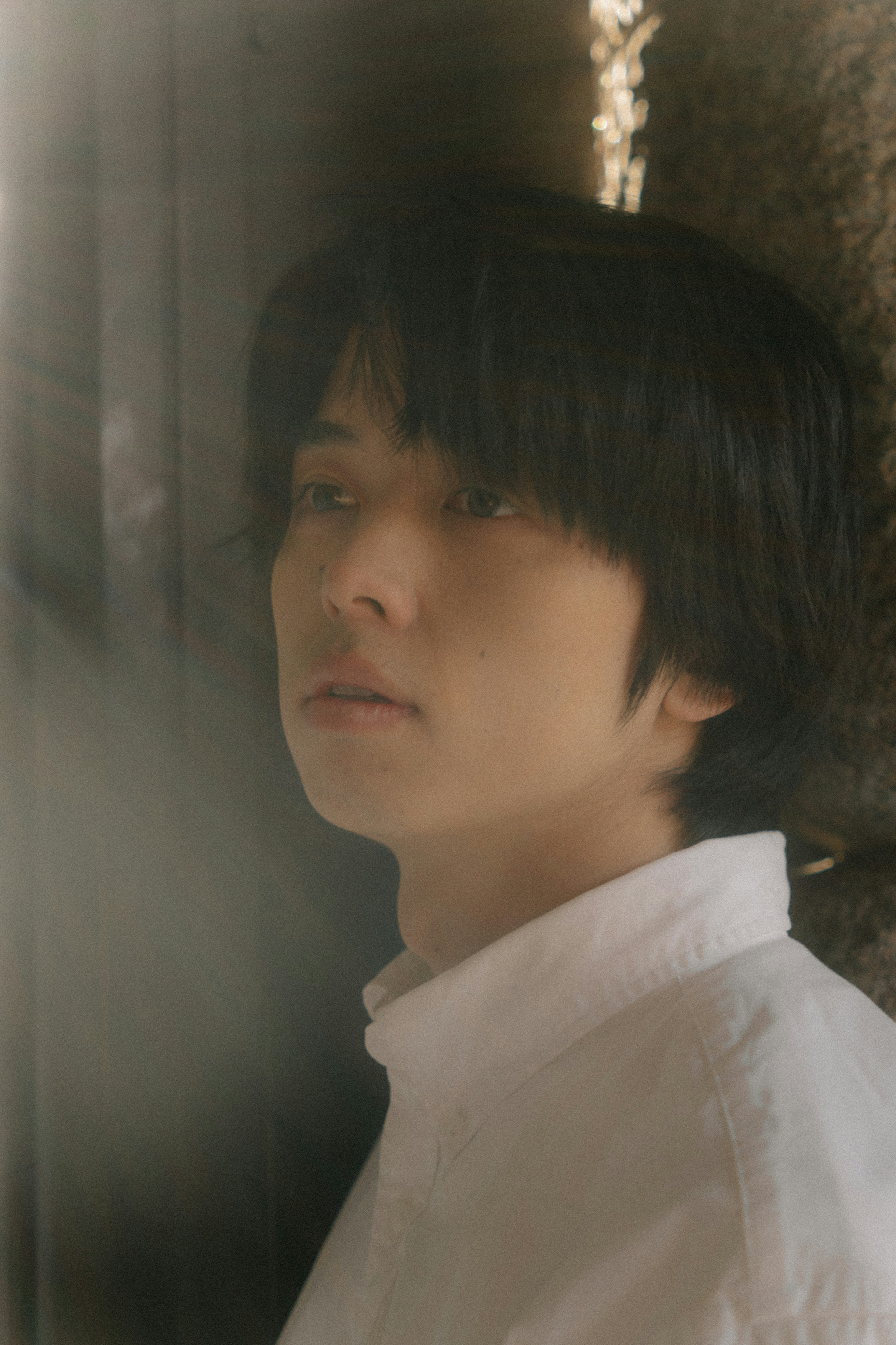 A young man wearing a white shirt leaning against a wall