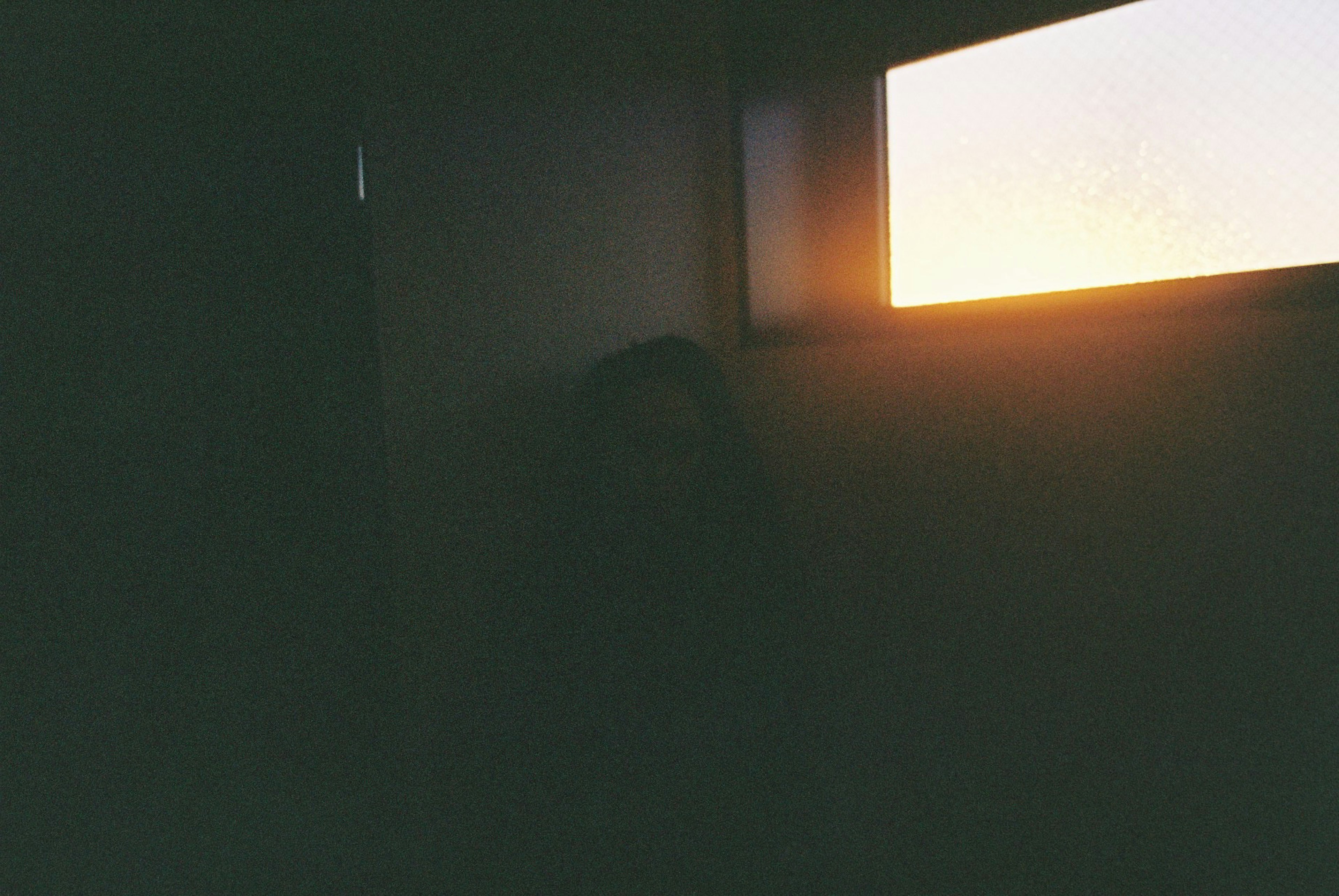 A person sitting in a dimly lit room with sunlight streaming through a window