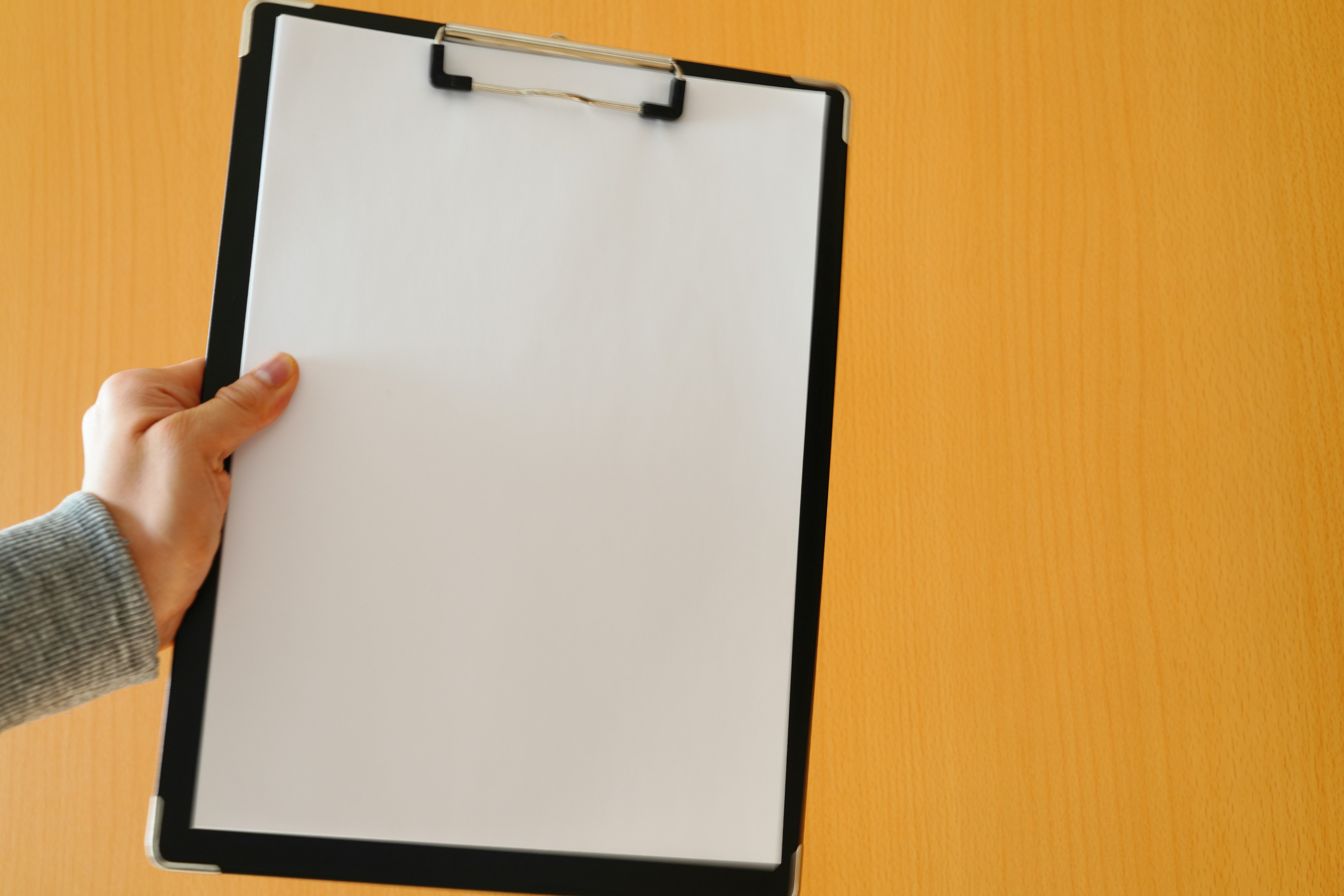 A hand holding a black clipboard against an orange wall