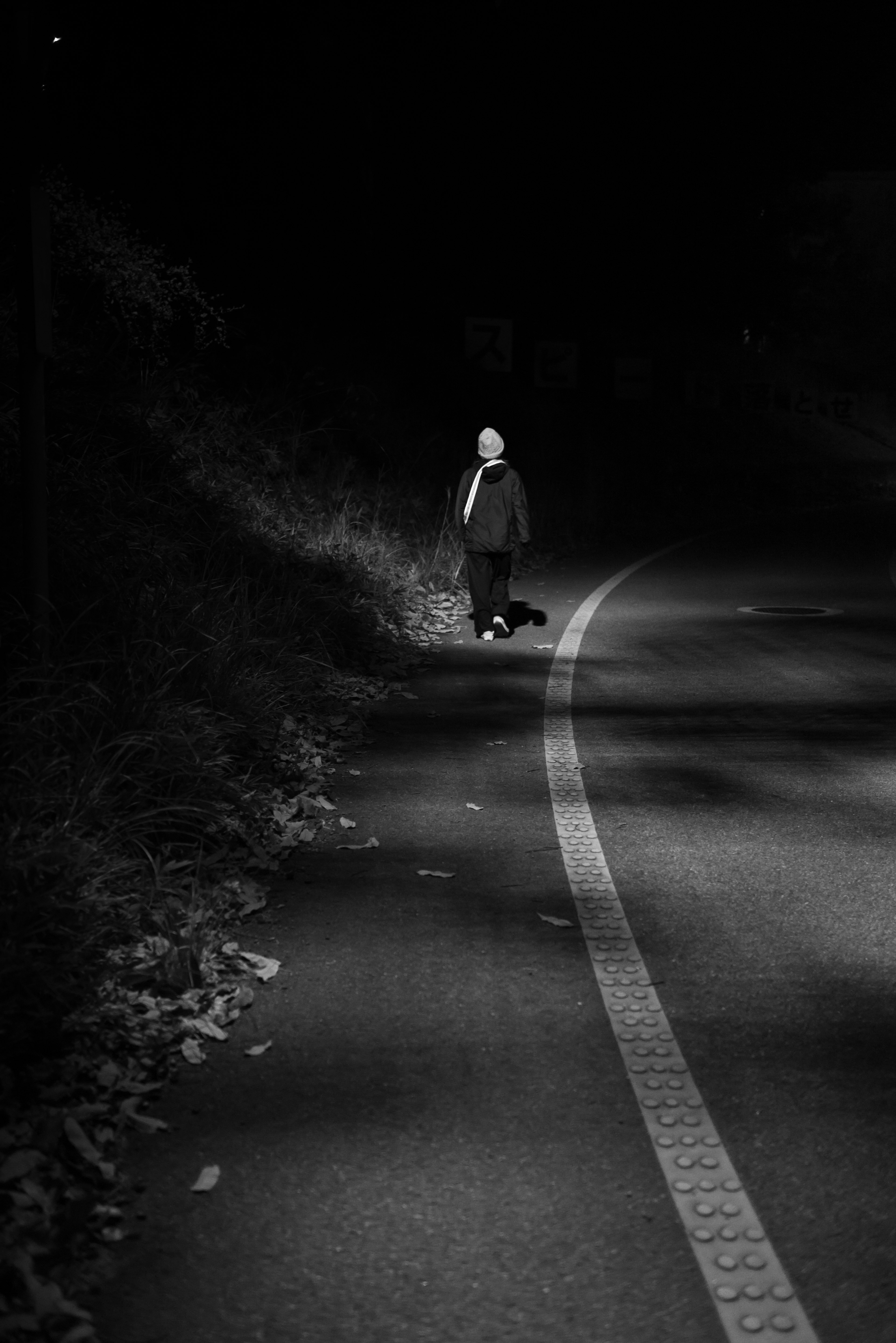 Photo en noir et blanc d'une personne marchant sur une route la nuit