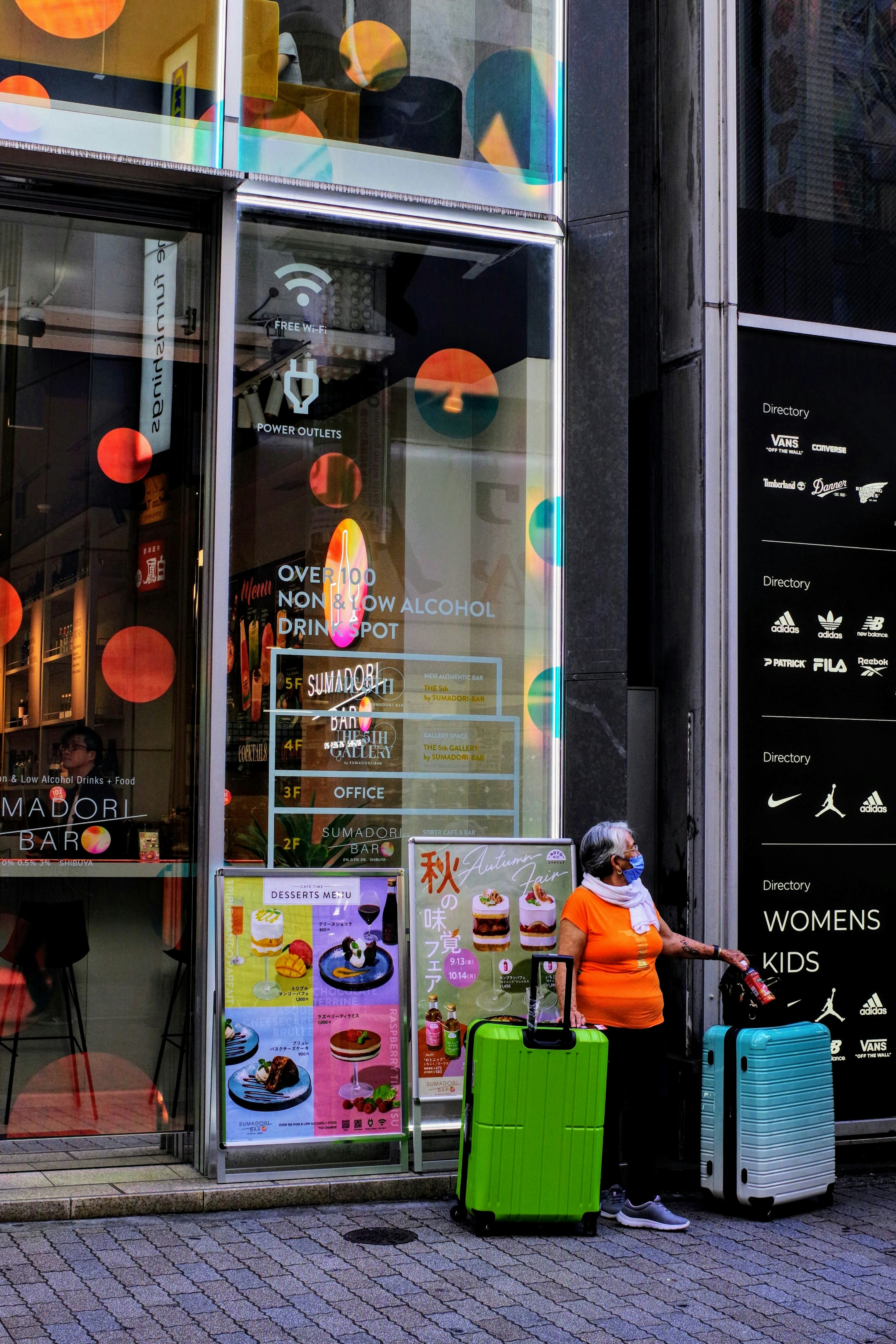 Person with luggage in front of colorful storefront with posters