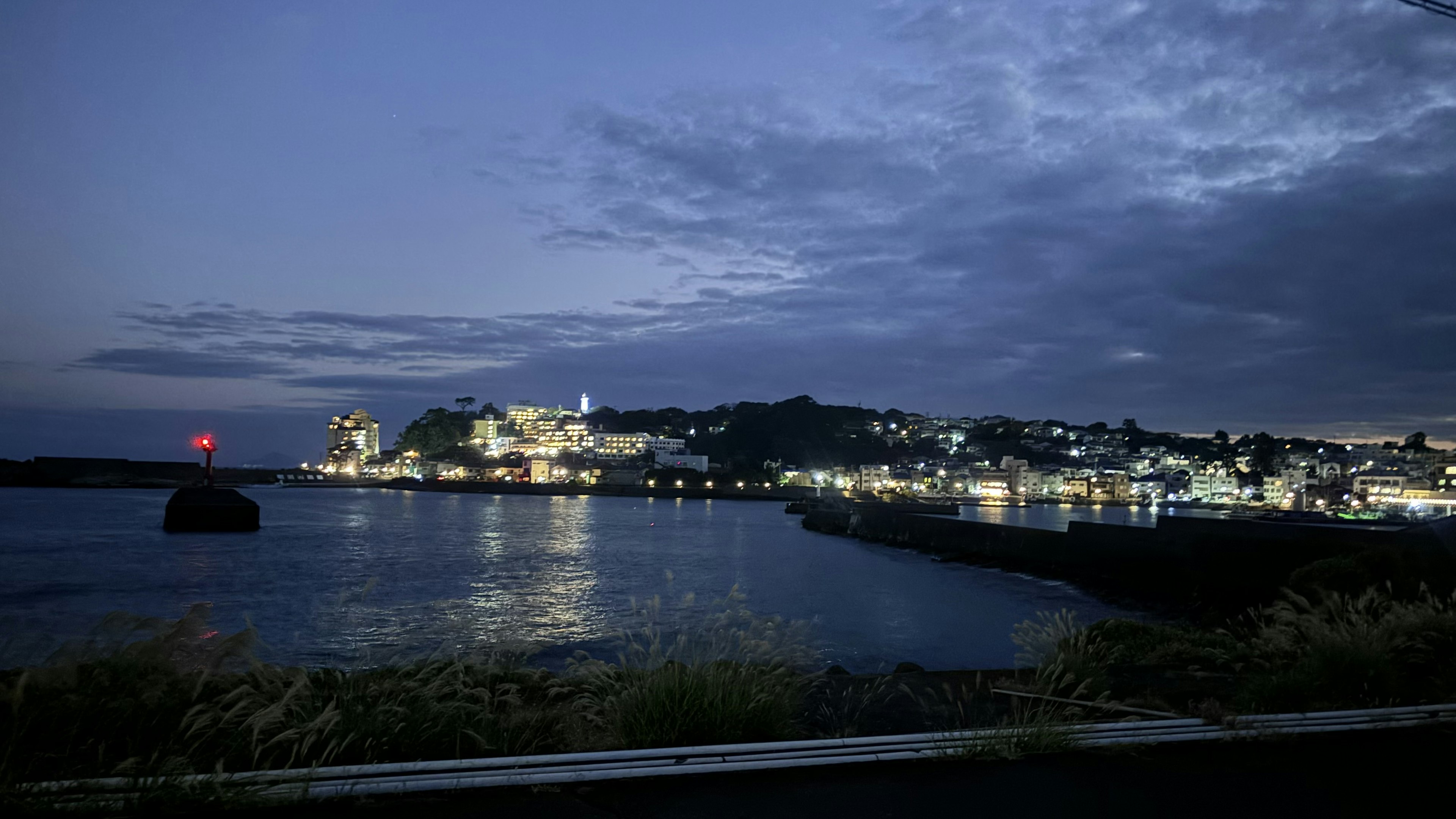 夜晚美丽的海岸城市景观 水面上的灯光反射和多云的天空